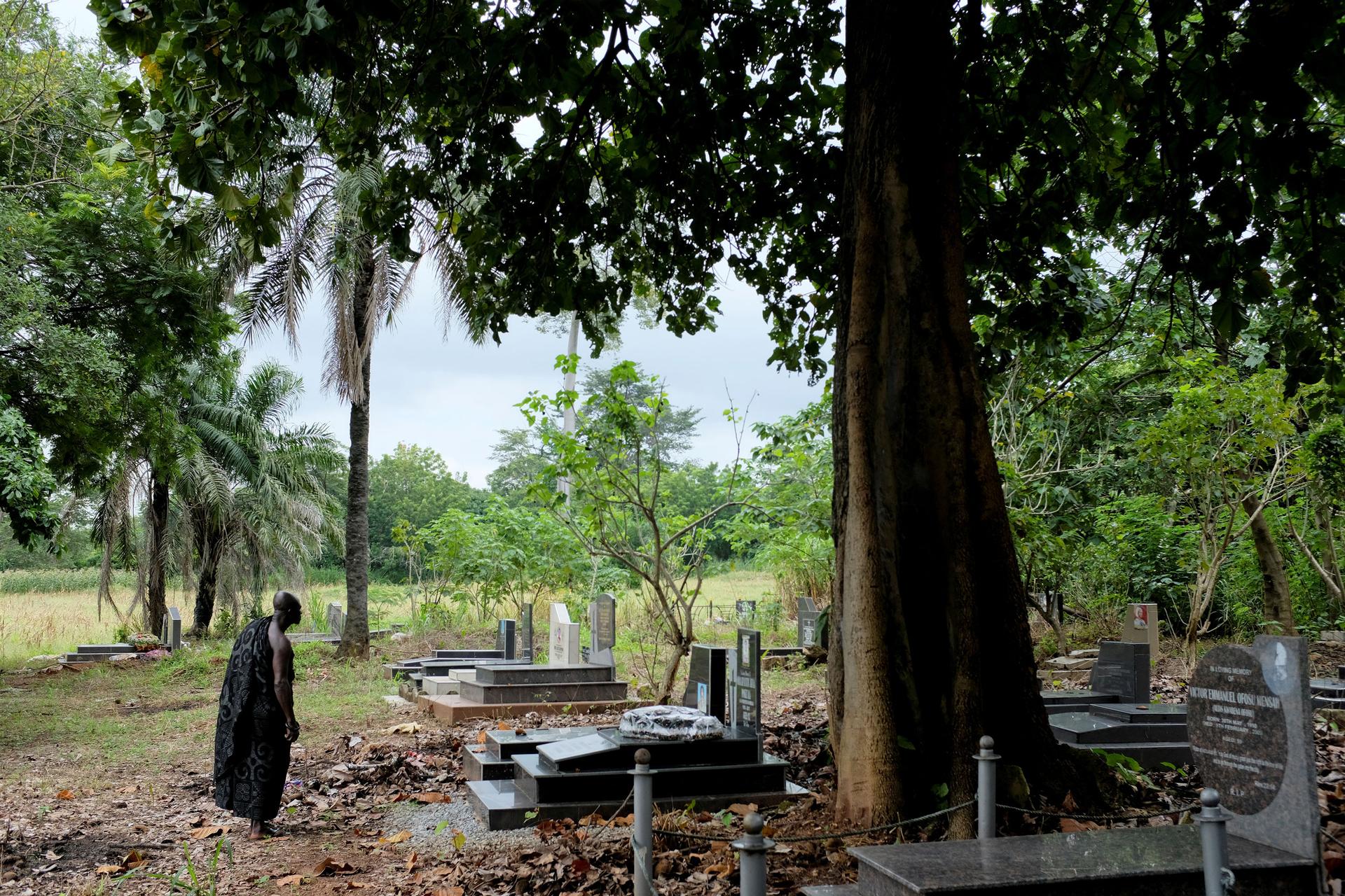 A grave yard is shown with a man standing looking at a long, rectangular marble tombstone.