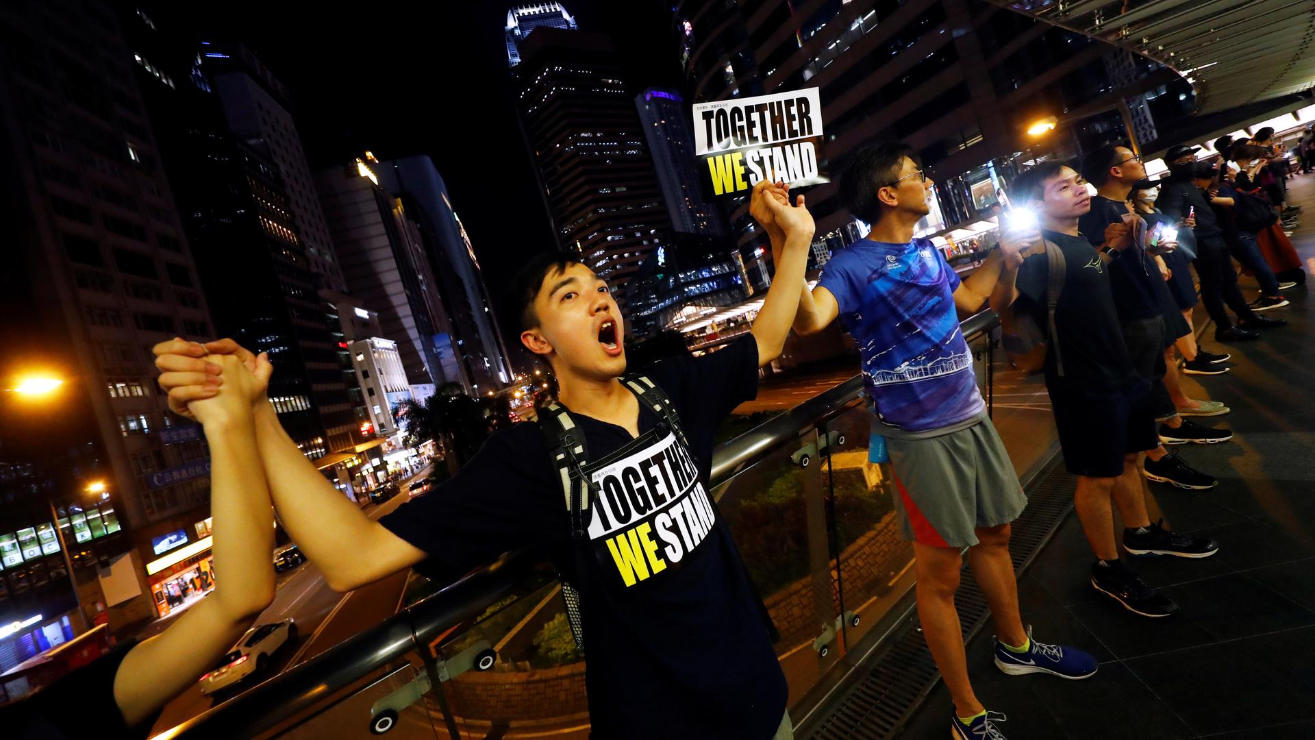 People stand holding hands and signs reading 'together we stand' in front of a nighttime cityscape