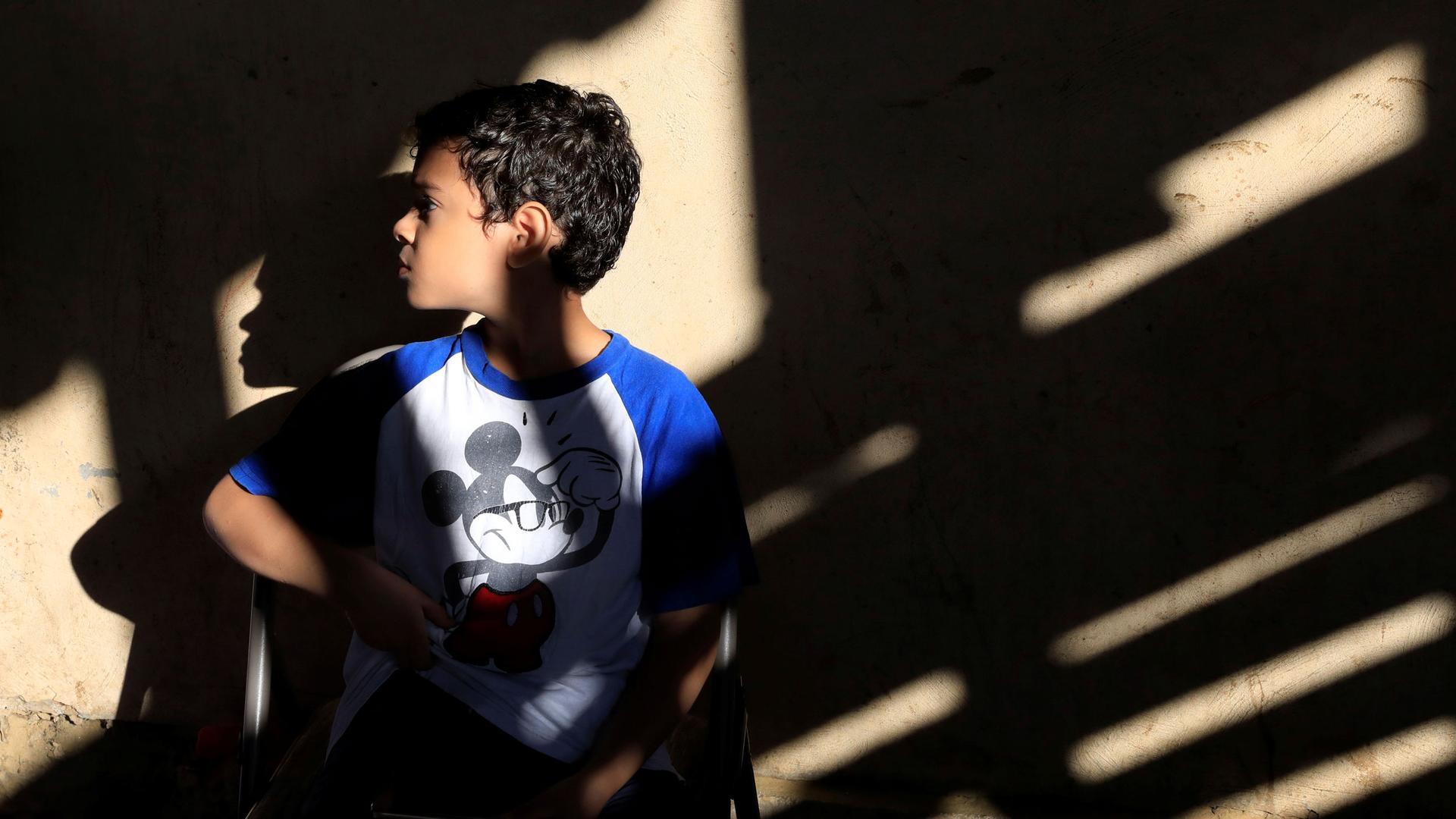 A young child is shown looking to his right and wearing a blue and white Mickey Mouse shirt.