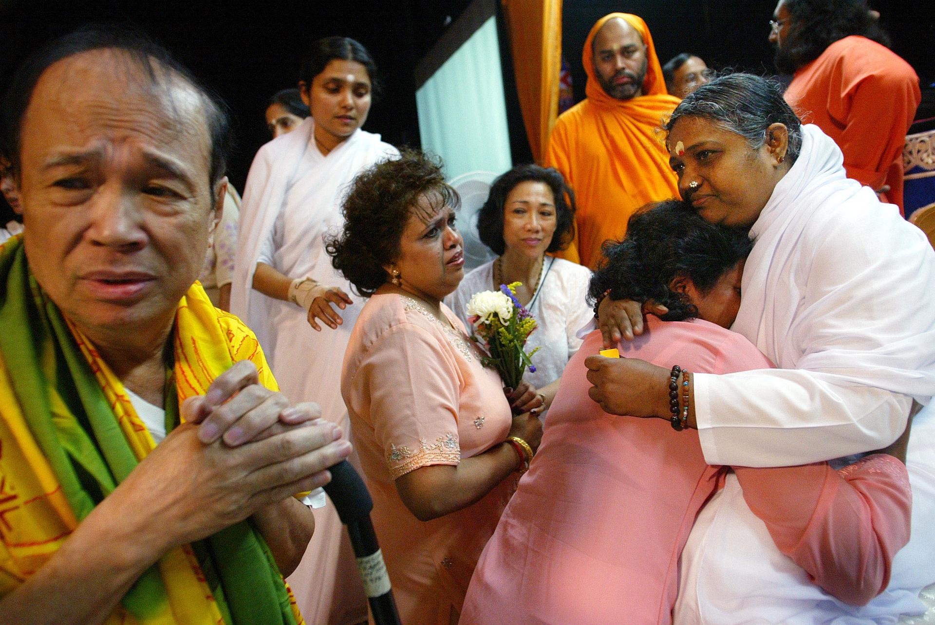Amma embraces a devotee surrounded by others in orange and white robes