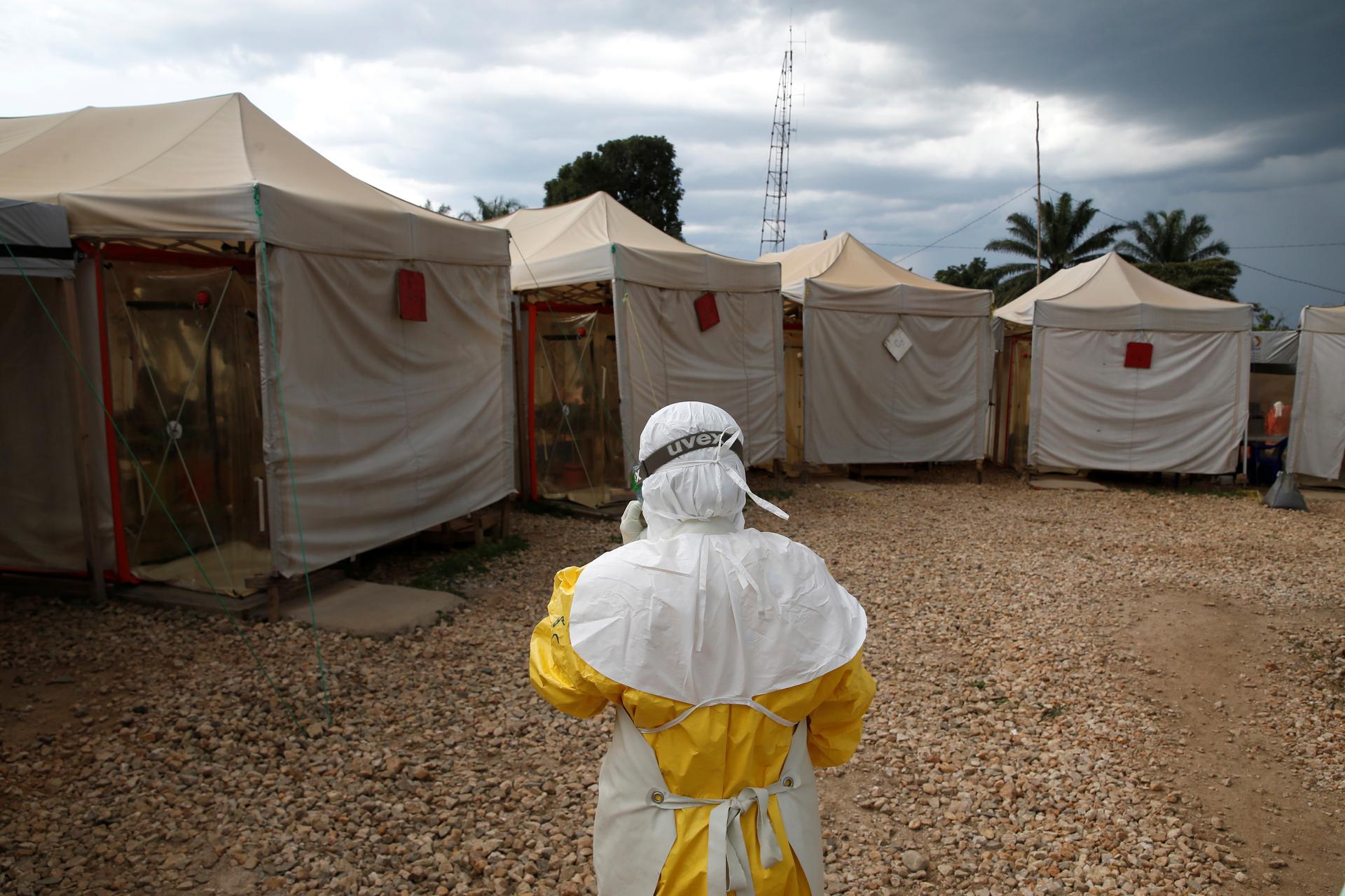 A health worker wearing Ebola protection gear walks next to tents.
