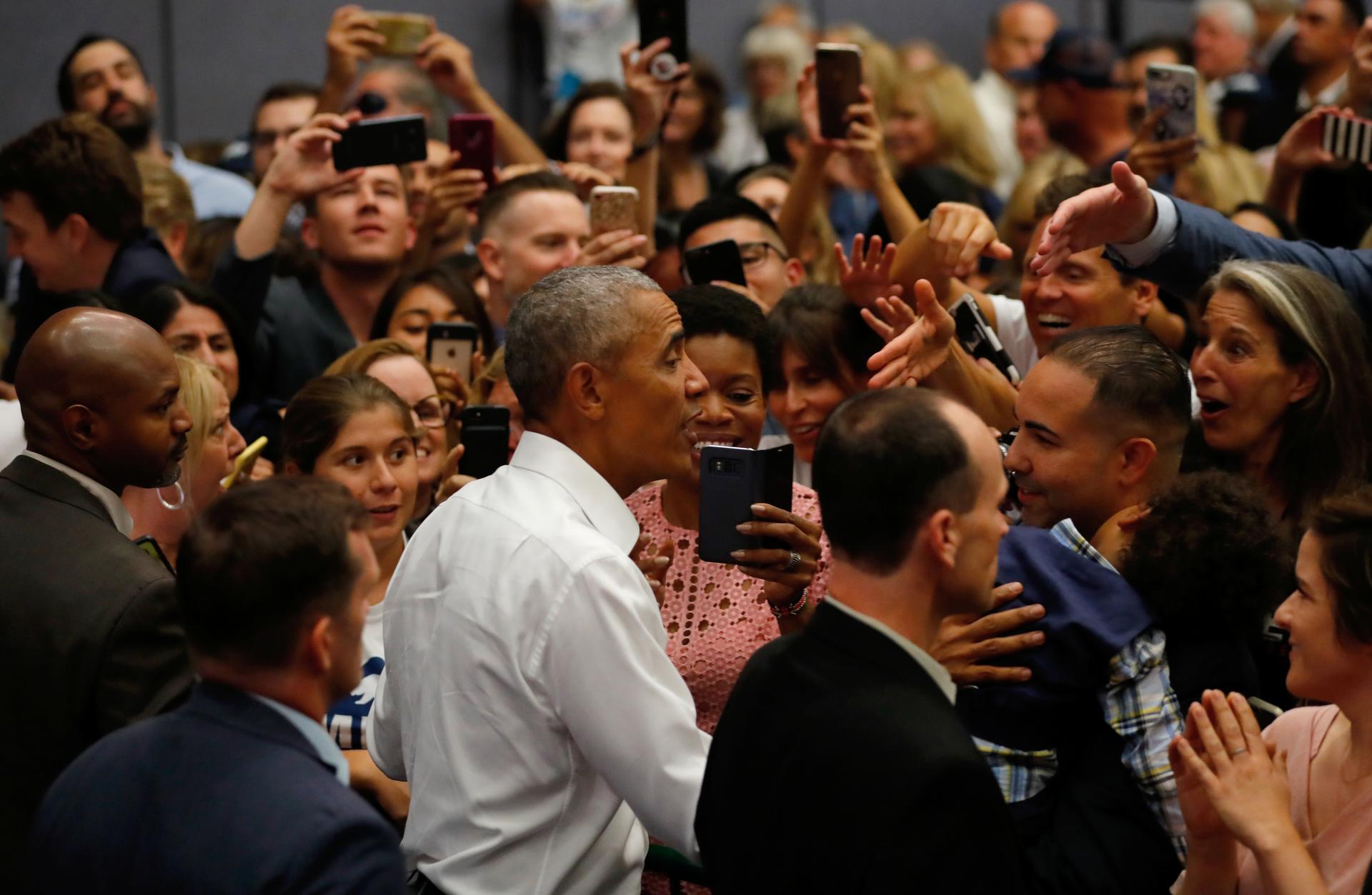 A large group of people surround former President Barack Obama