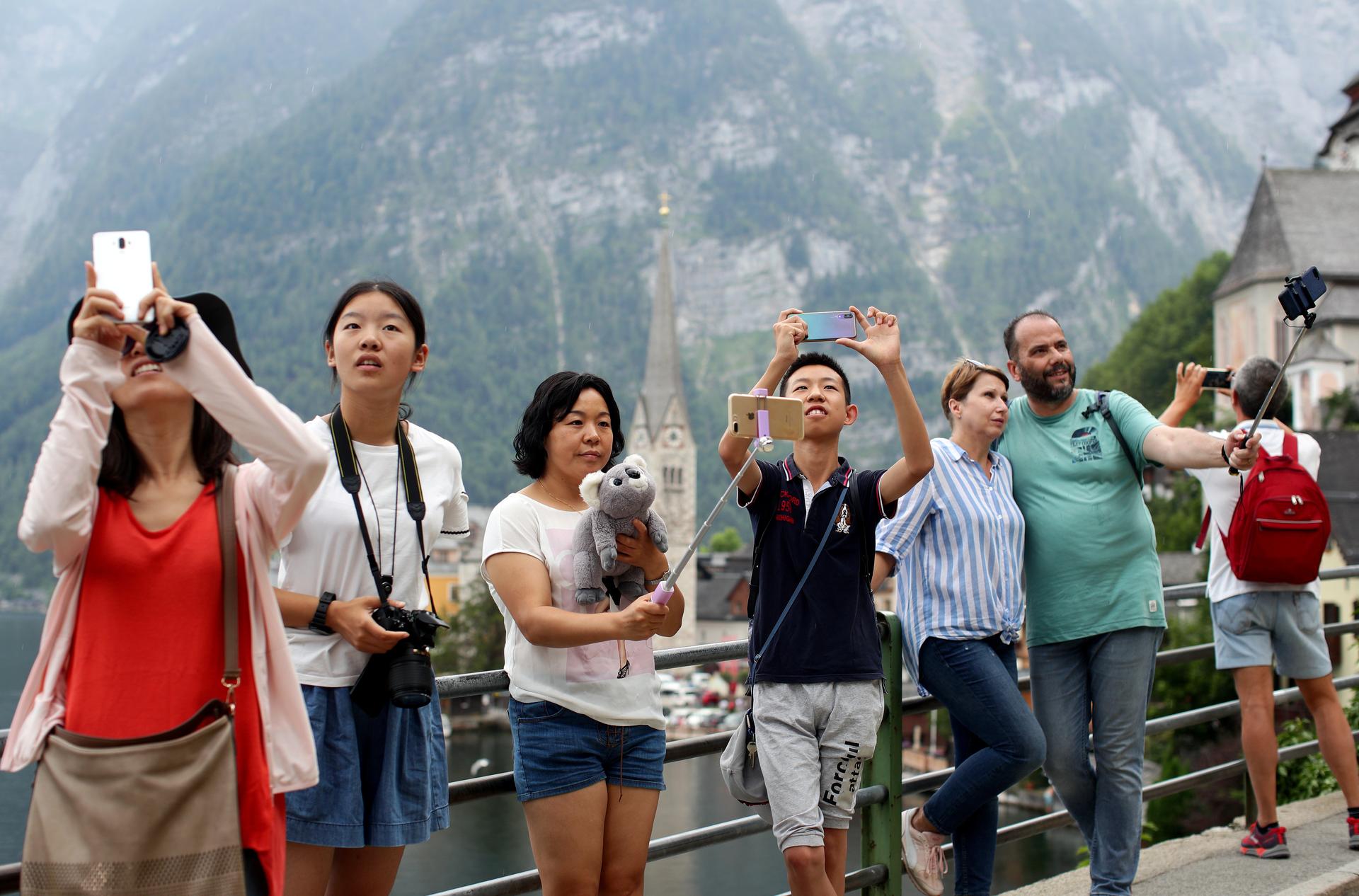 A group of tourists stands taking selfies outside.