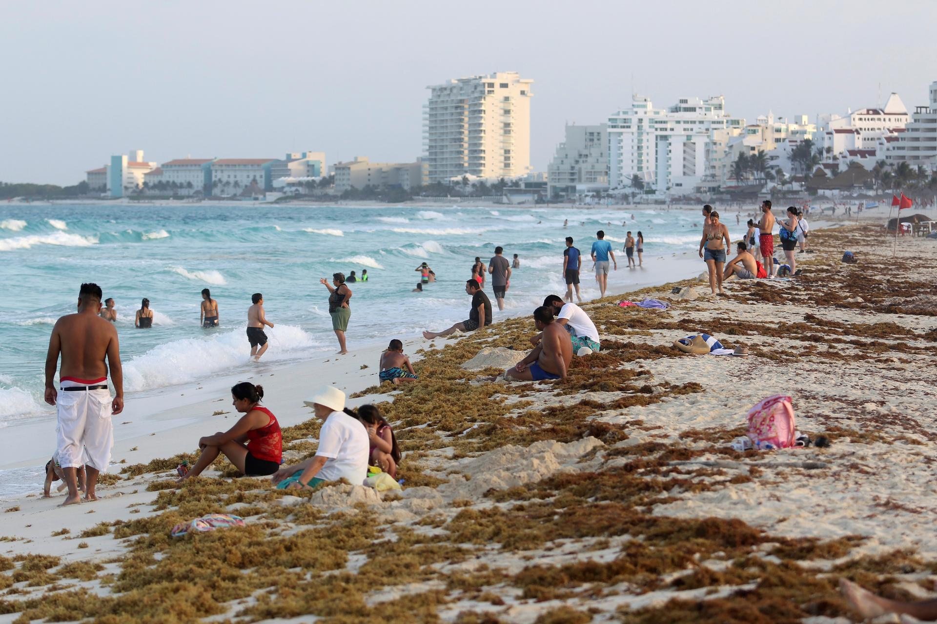 Tourists are seen on a beach covered with seaweed in Cancun.