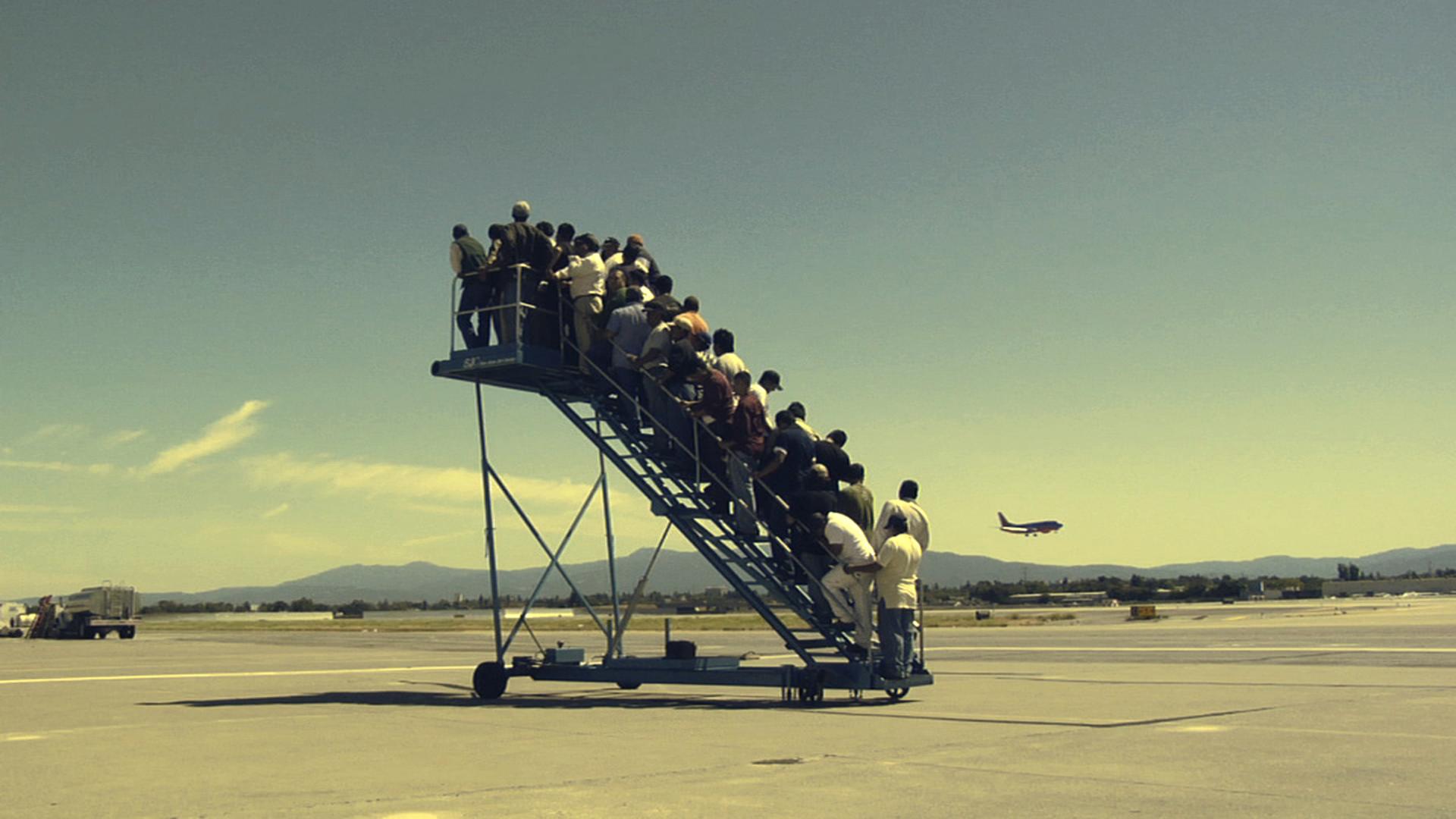 A group of people is seen on a mobile staircase at an airport. 