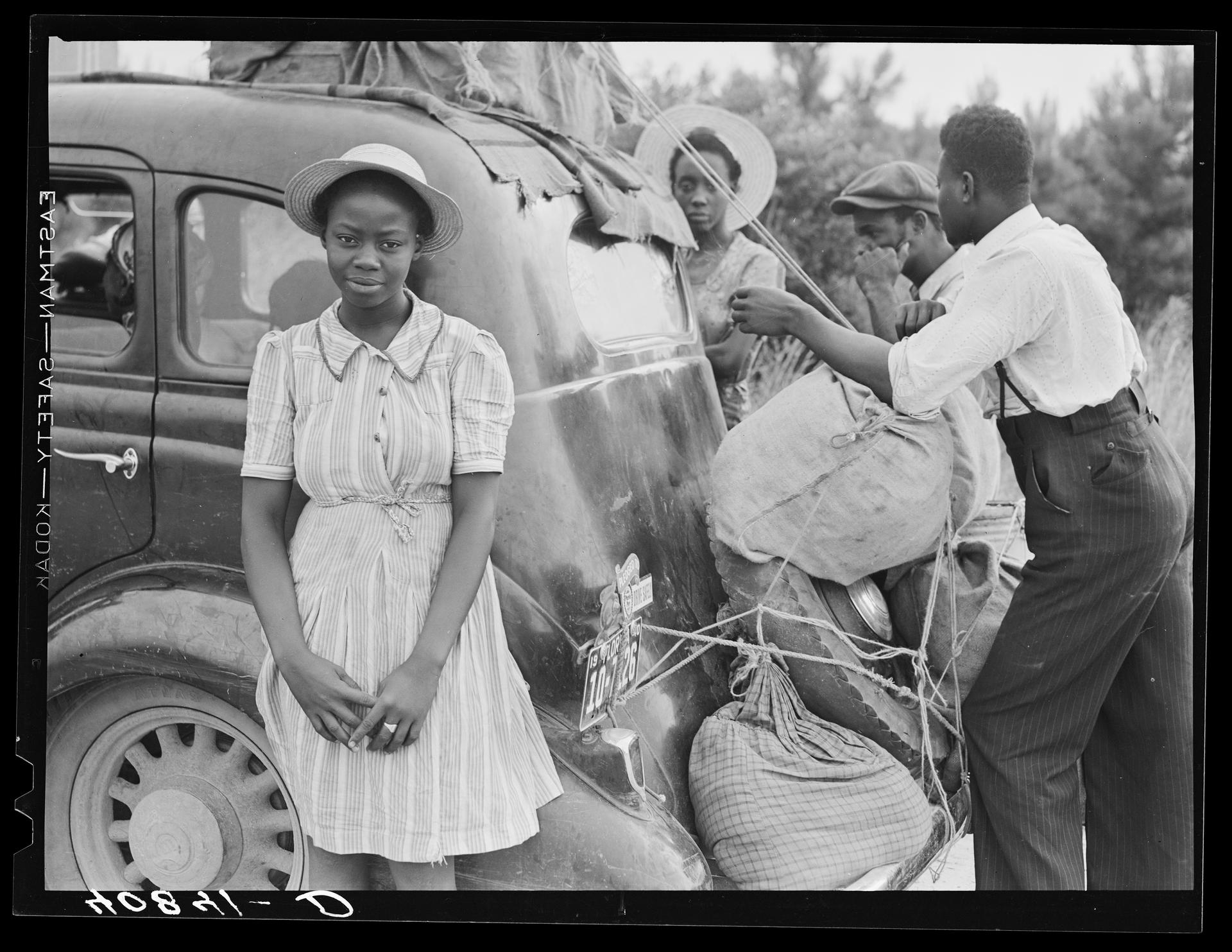 A family is seen tying sacks of potatoes to a car.
