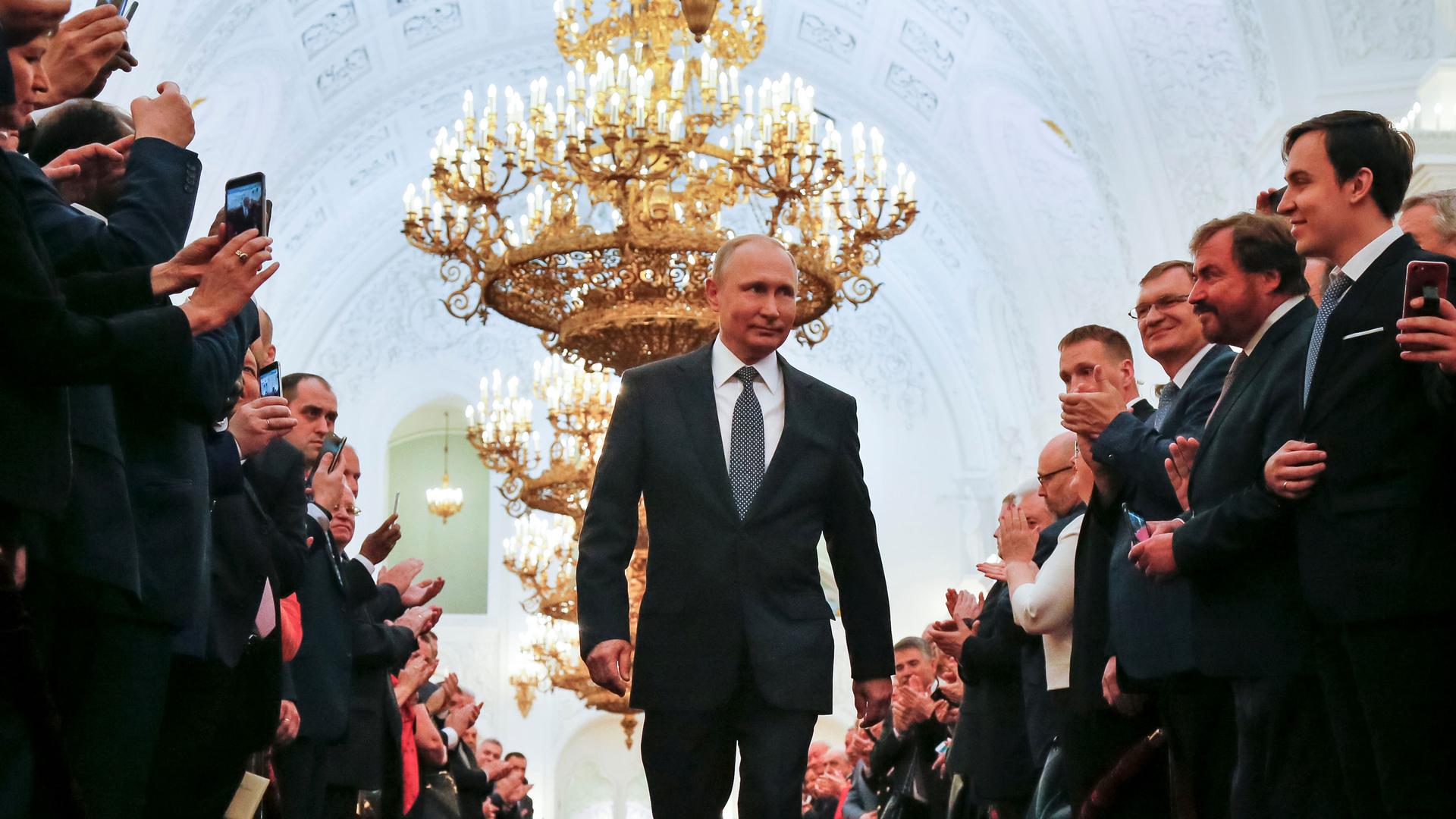Vladimir Putin walks between two rows of people clapping their hands and taking photos with their cell phones