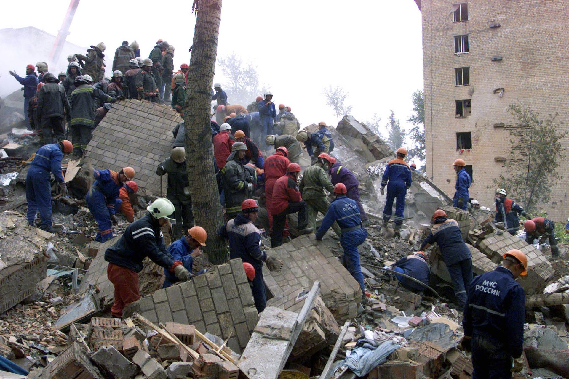 A crowd of people wearing hard hats shift through the rubble of a building