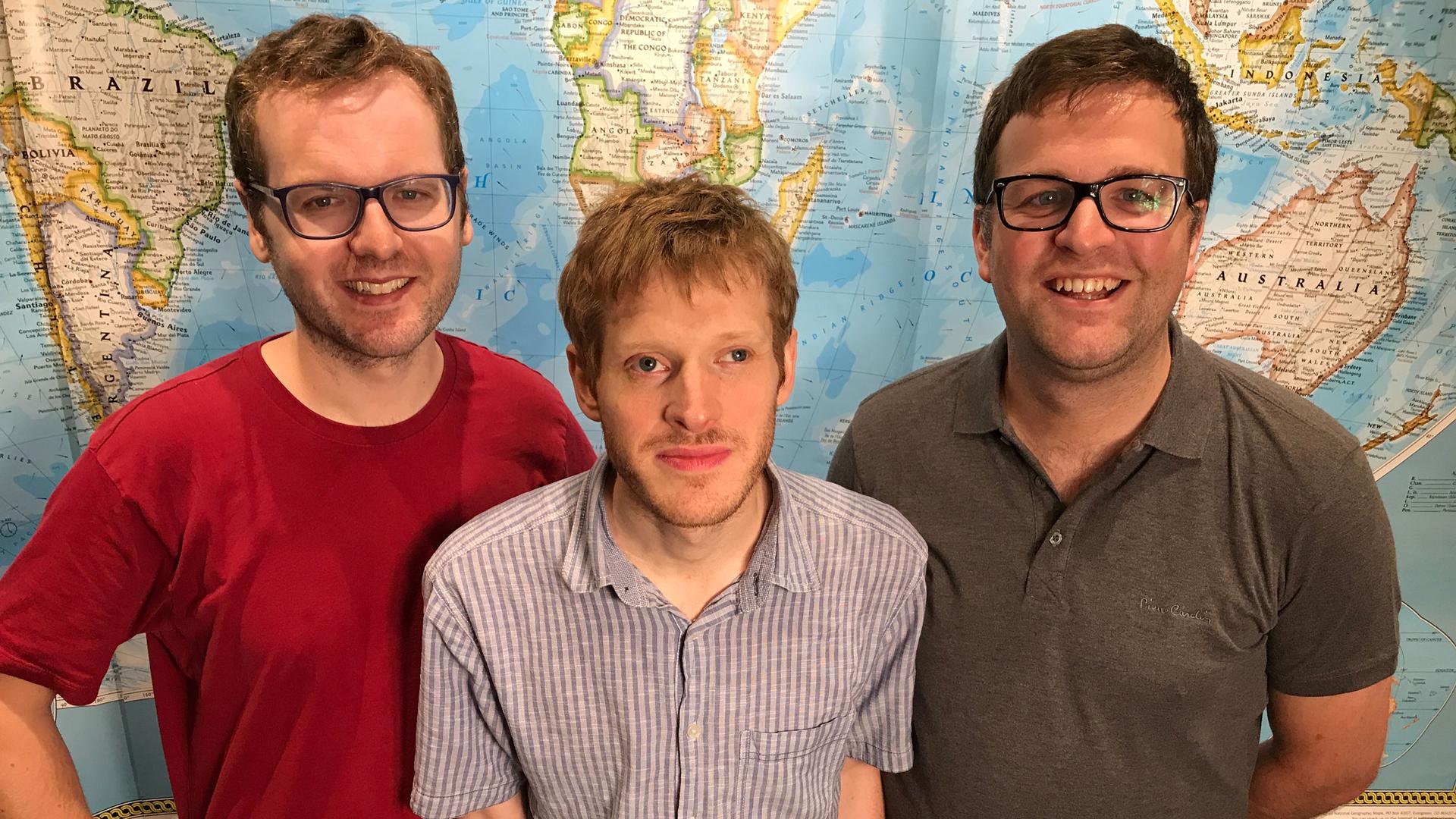 A group of three men are photographed against a world map