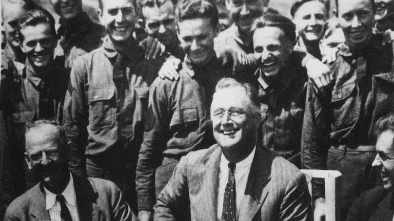 President Franklin Roosevelt poses for a photo with other men behind him in a historical image