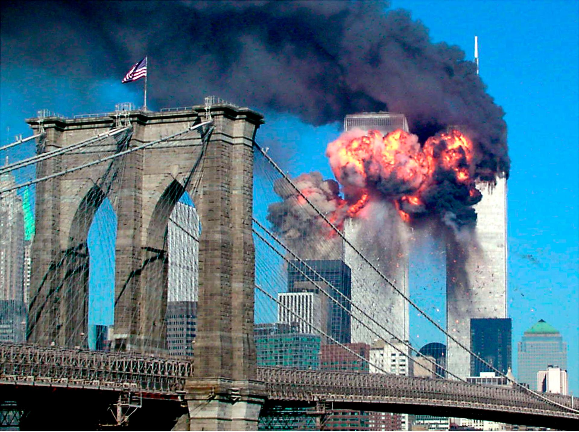 The second tower of the World Trade Centre explodes after being hit by a hijacked airplane. A bridge with an American flag flying is in the foreground.