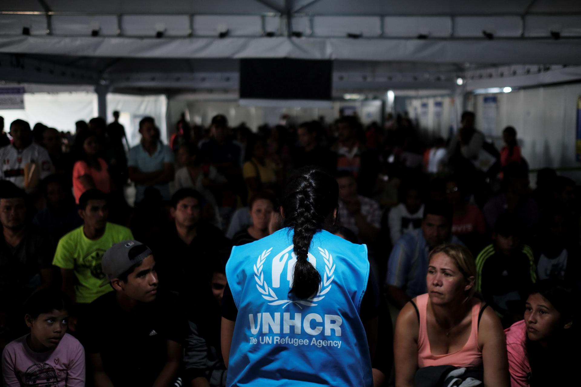 A member of United Nations High Commissioner for Refugees (UNHCR) talks with Venezuelans as they queue in line to receive a vaccine after showing their passports or identity cards at the Pacaraima border control, Roraima state, Brazil, on Aug. 8, 2018. 