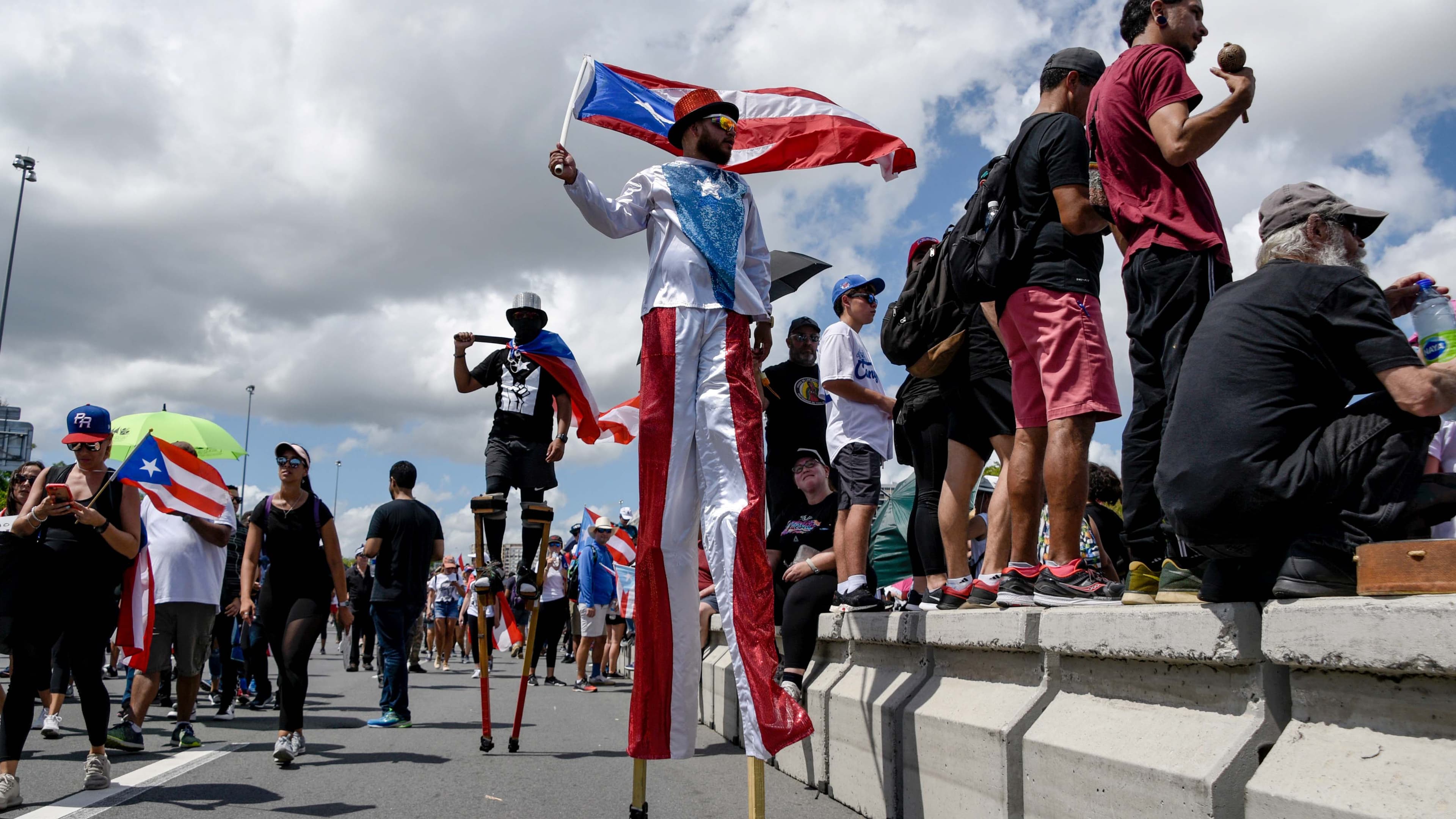 Several people on stilts and others line a street