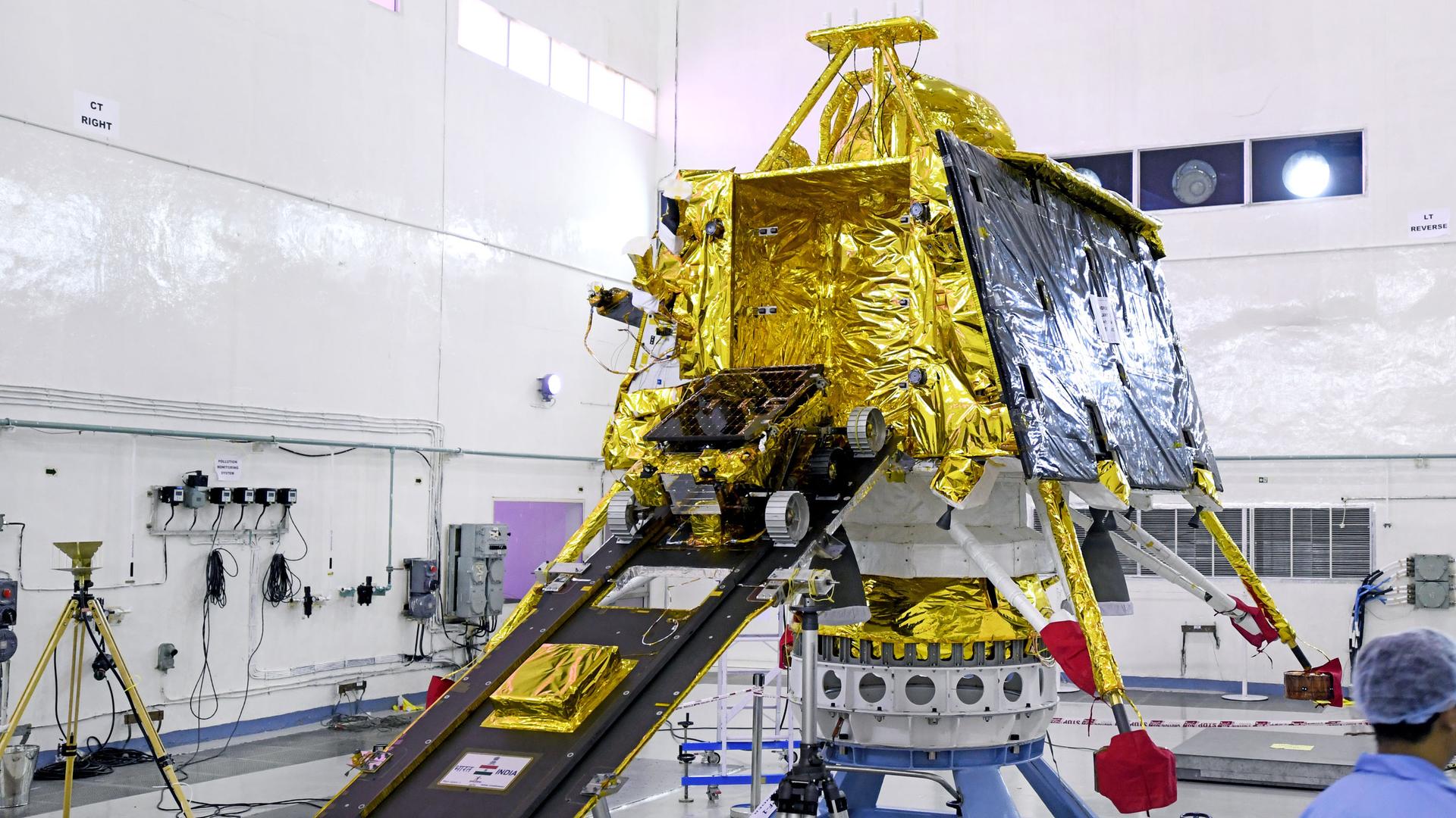 A small rover exits a large, gold spacecraft.