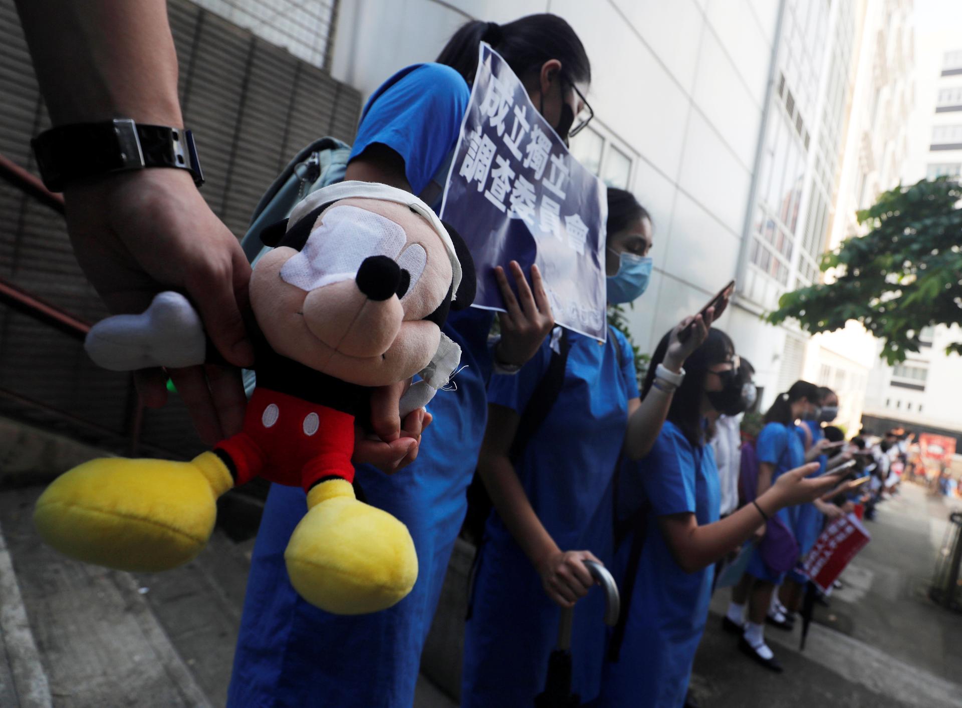 Secondary school students hold a Mickey Mouse stuffed doll with an eye patch as they form a human chain