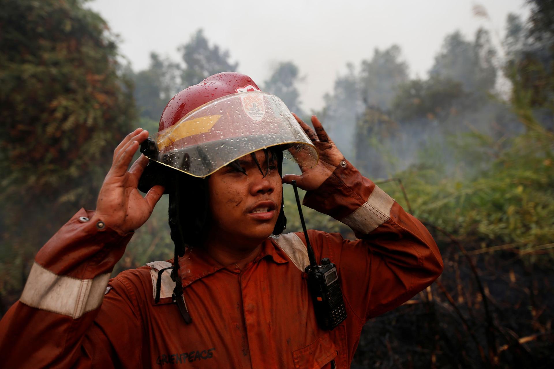 A man is shown with his hands rised to the brim of his fire helmet.