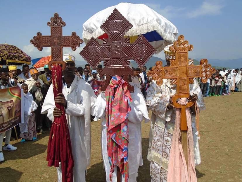 Three people hold large Ethiopian crosses as they walk down the street