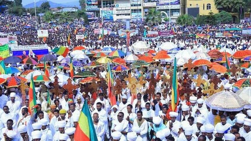 A mass of protesters wearing white and carrying Ethiopian flags gather in the street 