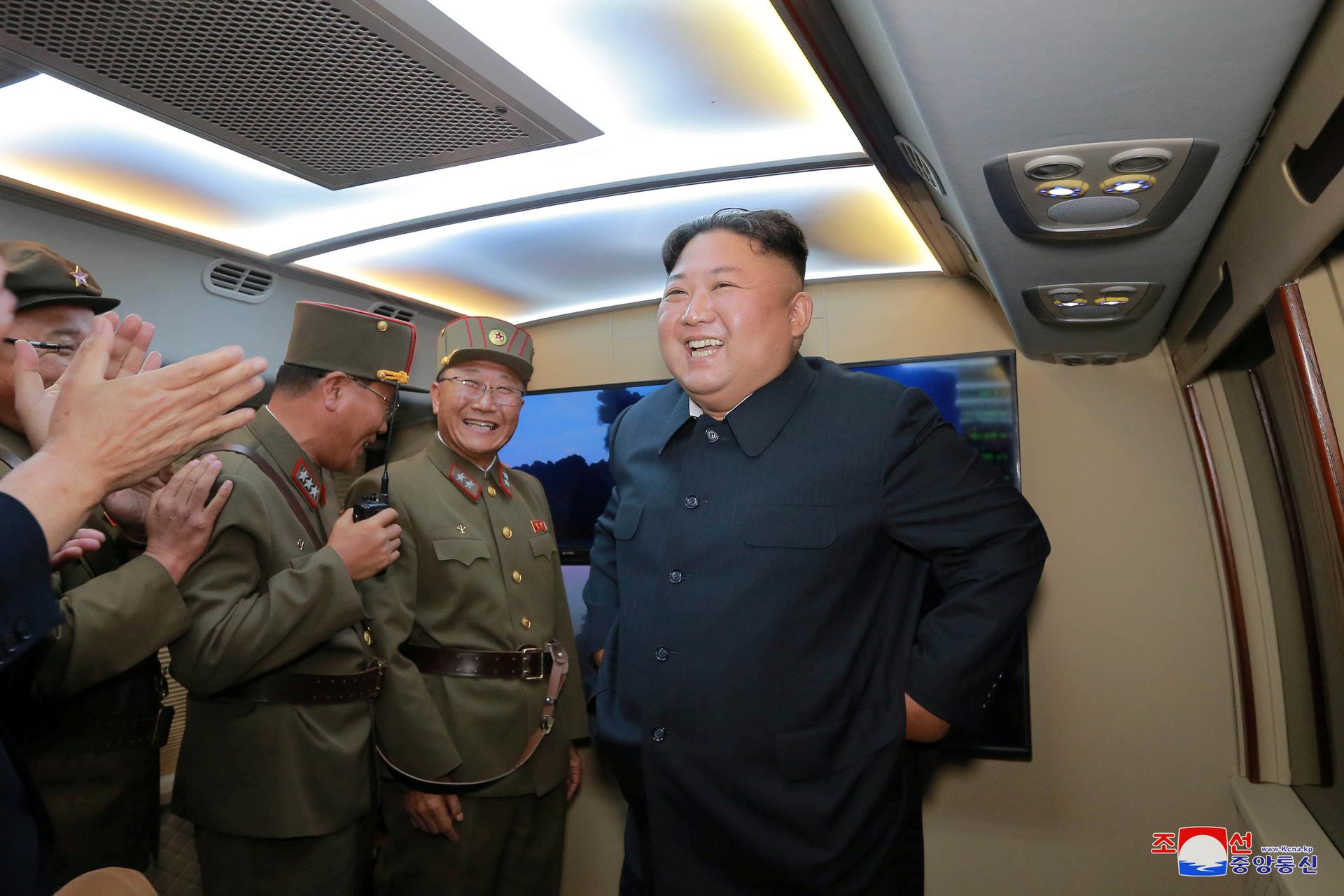 Kim Jong-un smiles in gray suit as he talks with men in green military uniforms