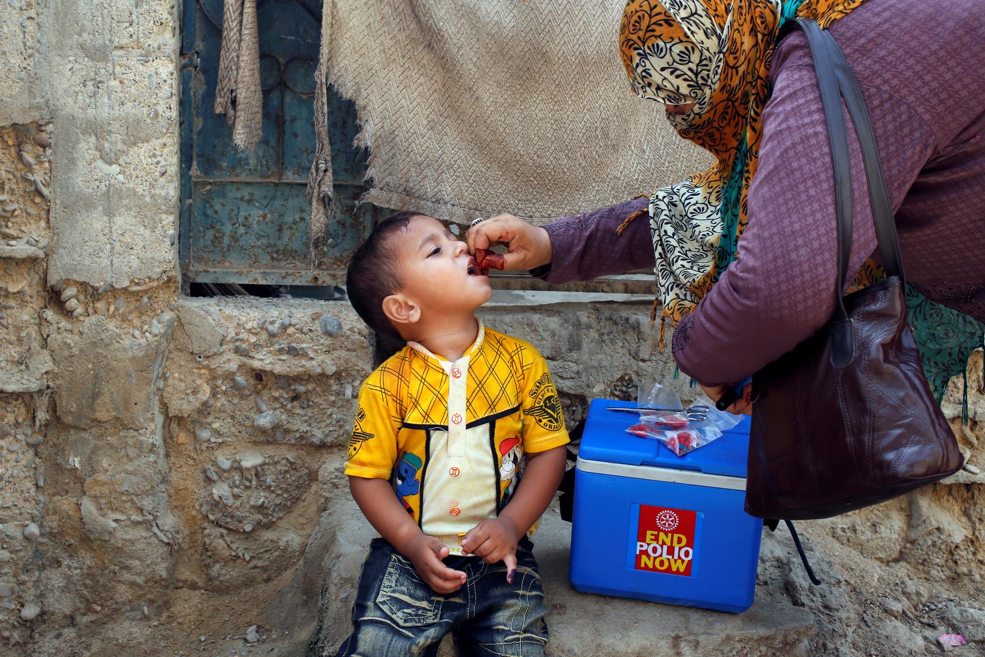 A woman gives a boy an oral polio vaccine.
