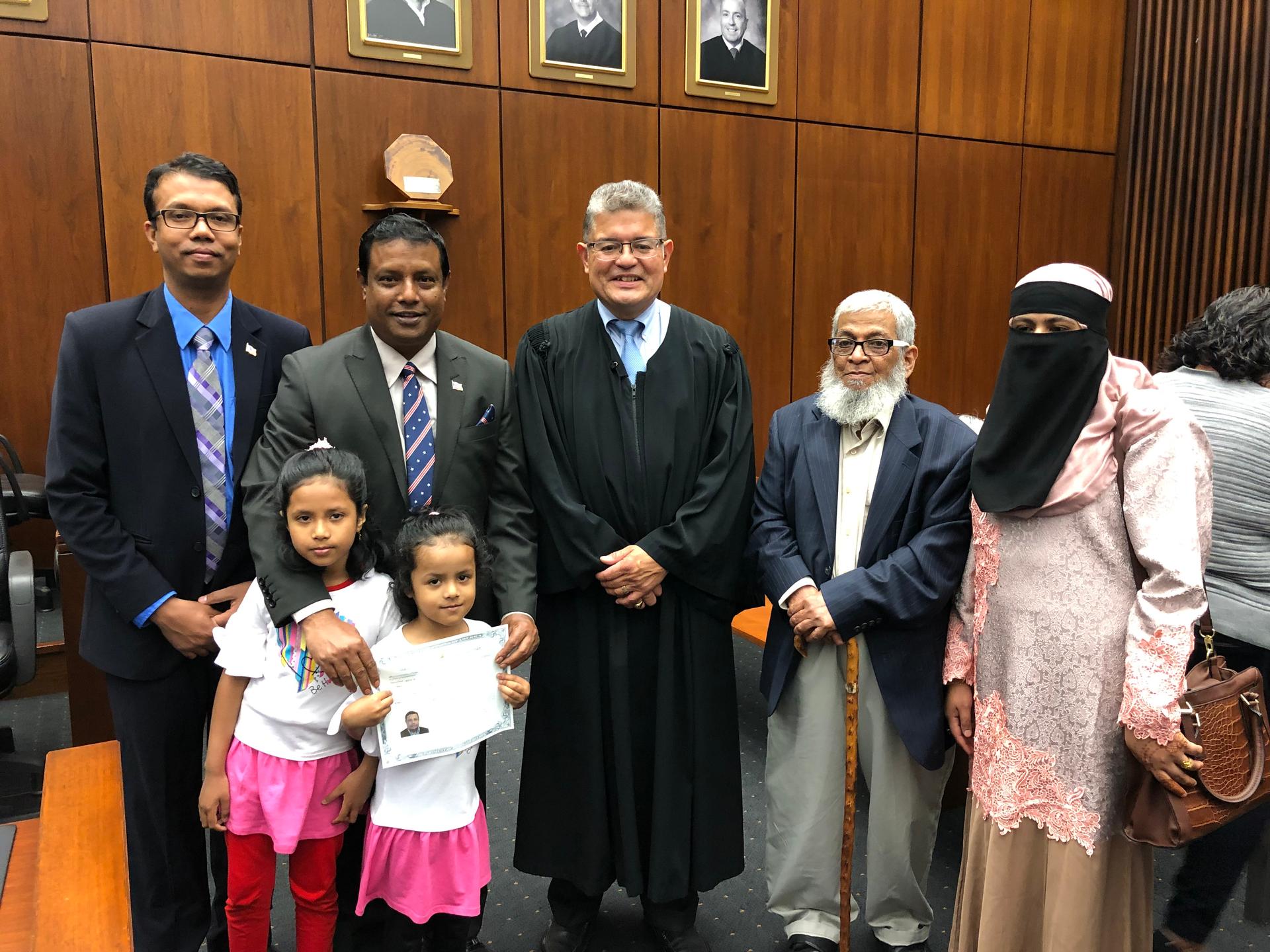 A man stands alongside a judge and his family at his naturalization ceremony.