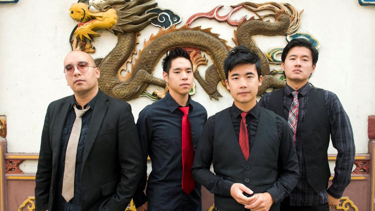 Four young men pose for a photo in front of a wall with the painting of a dragon.