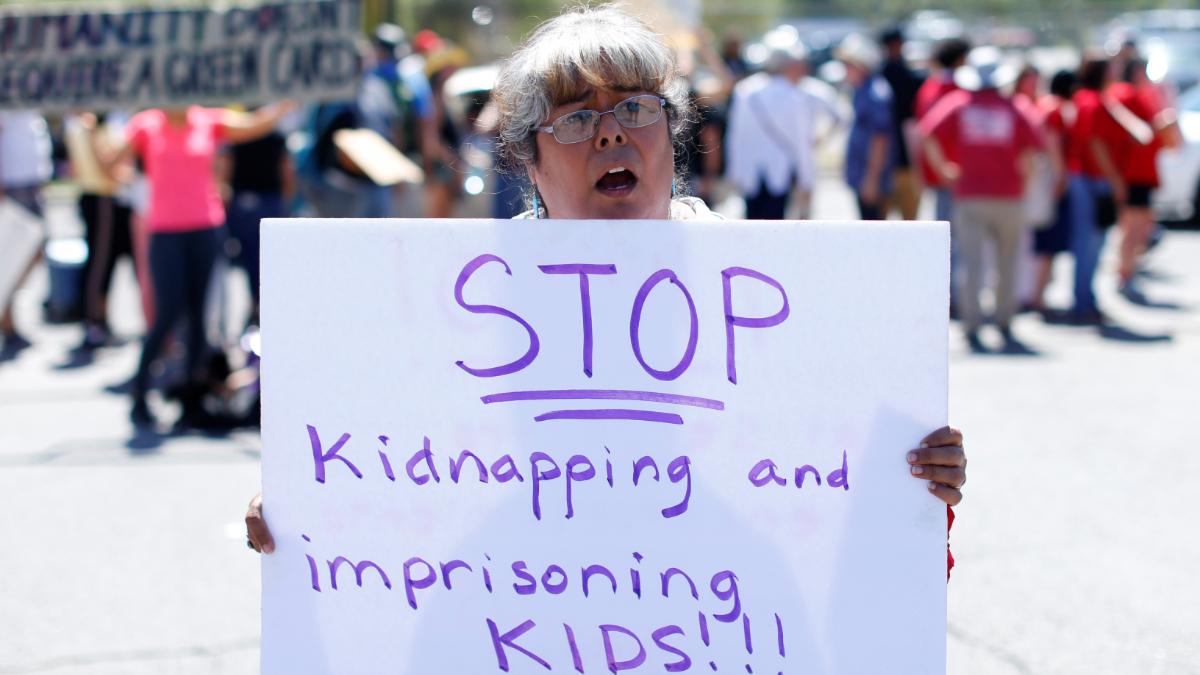 A woman hold a sign that reads, "stop kidnaping and imprisoning kids."