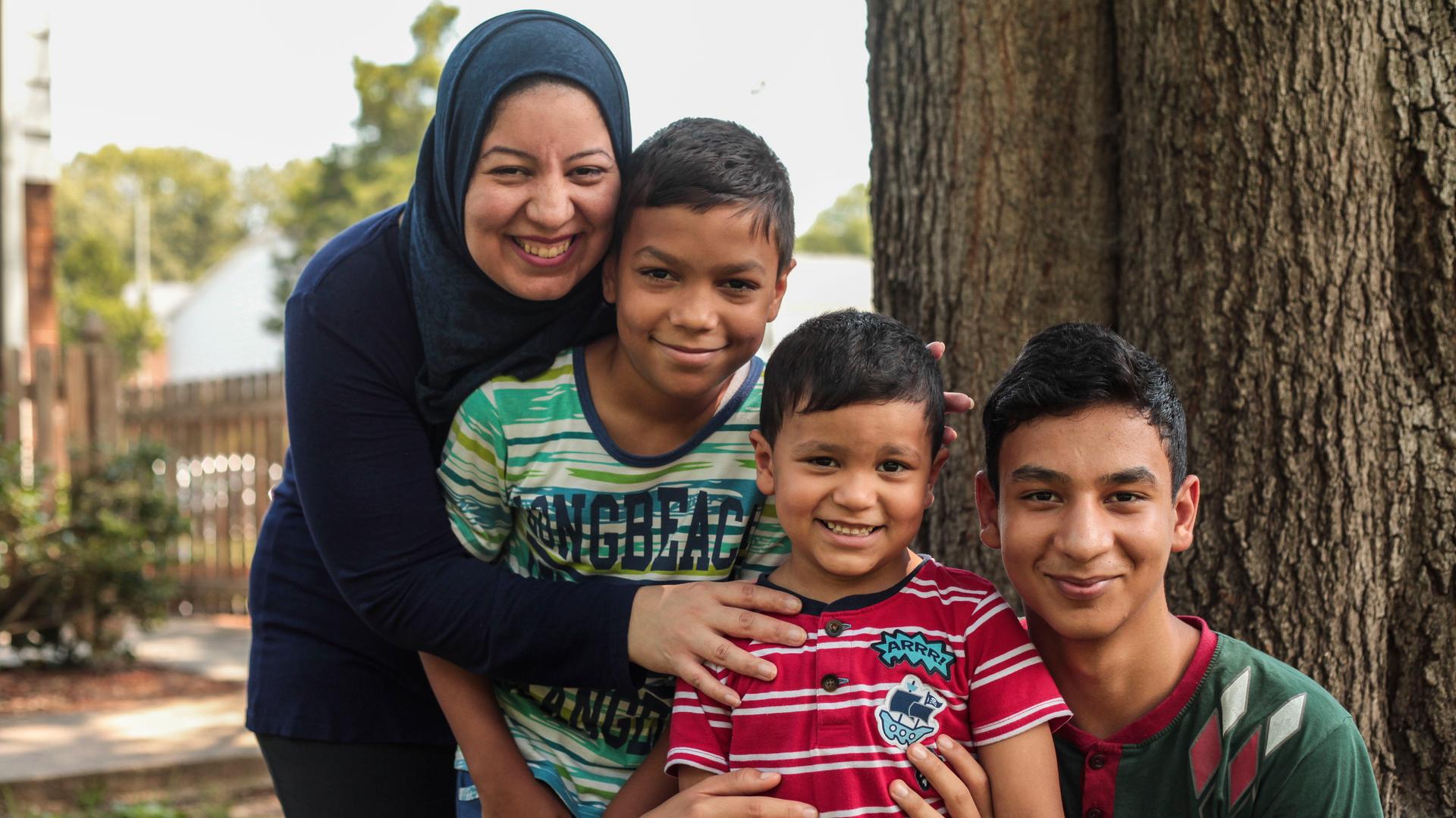 A woman in a hijab smiles and poses with three boys ranging in age 