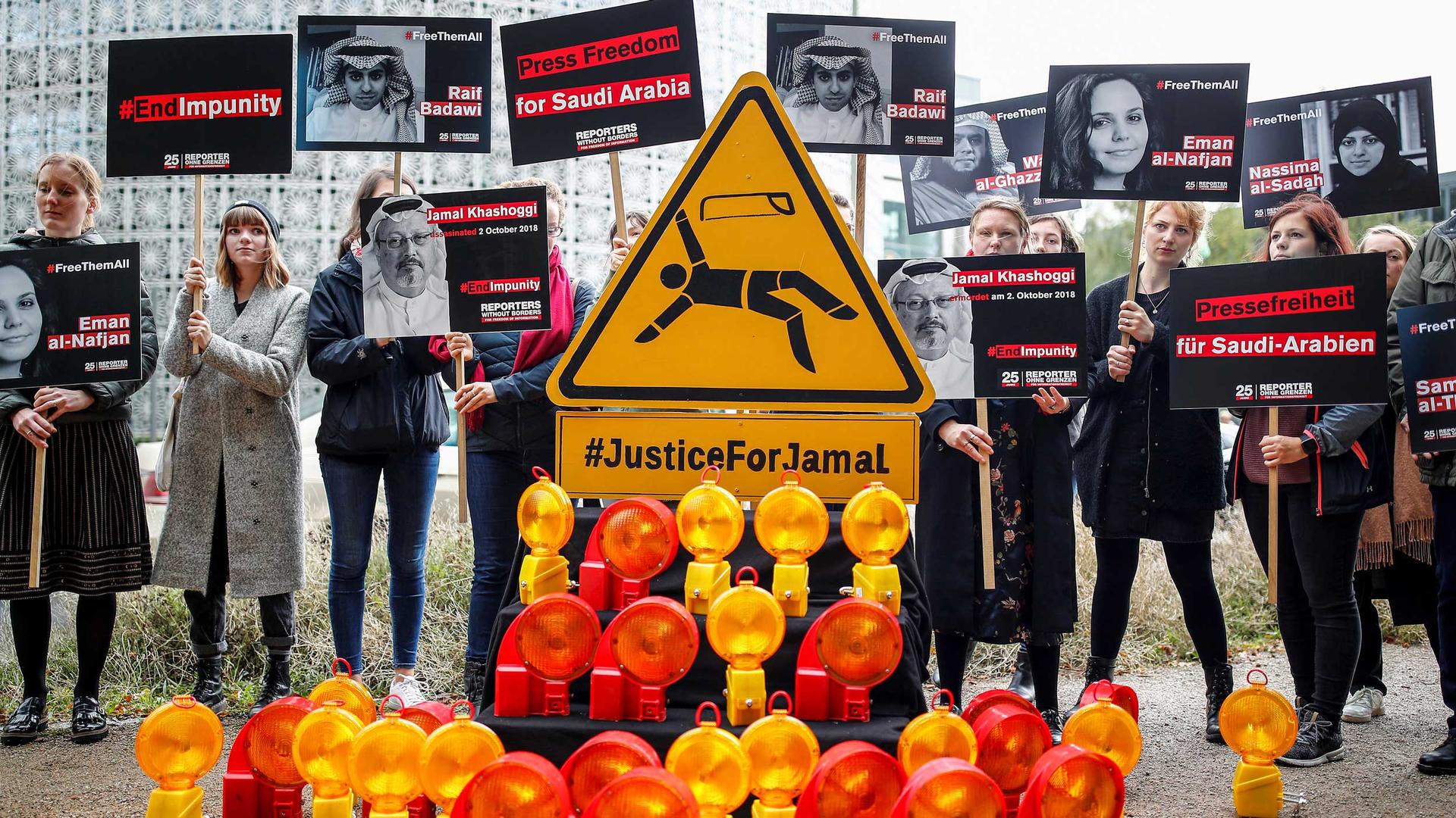 Protesters hold signs with images of Saudi journalists on them