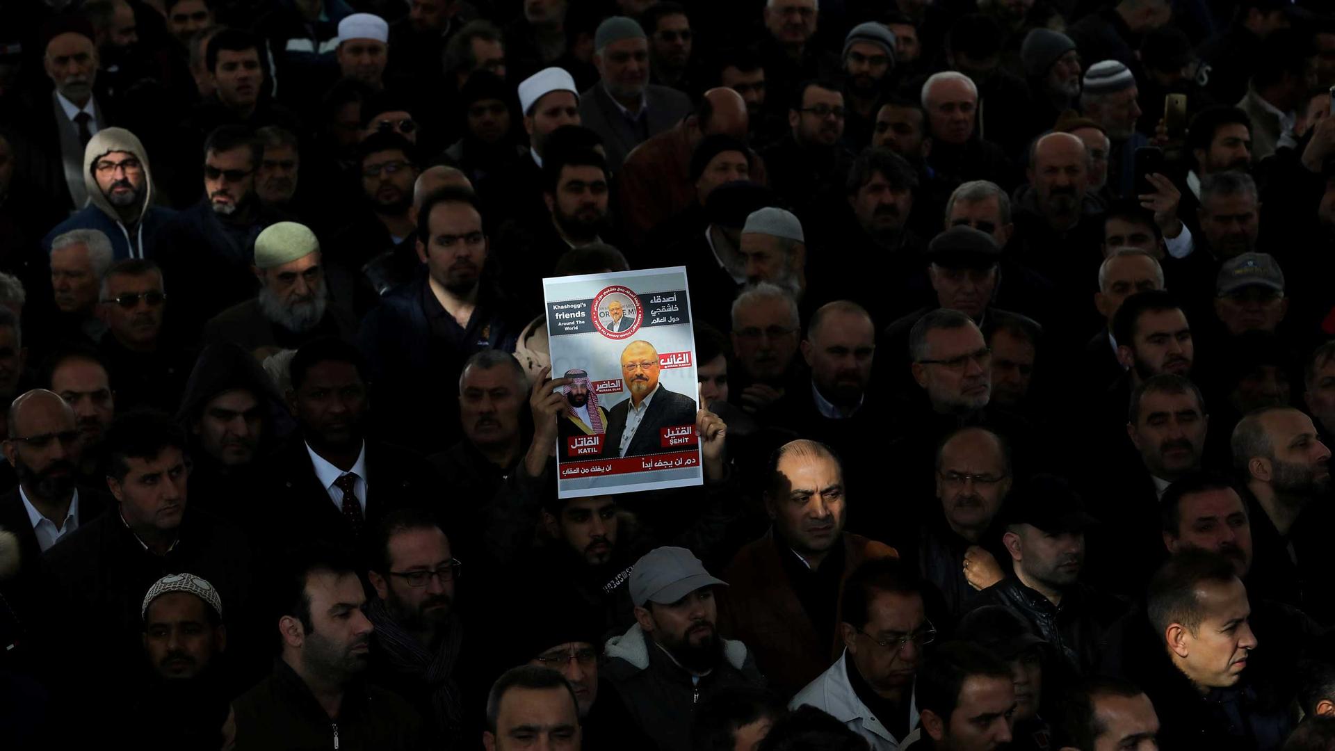 Dozens of people are praying and one person holds up a sign with Jamal Khashoggi's image on it