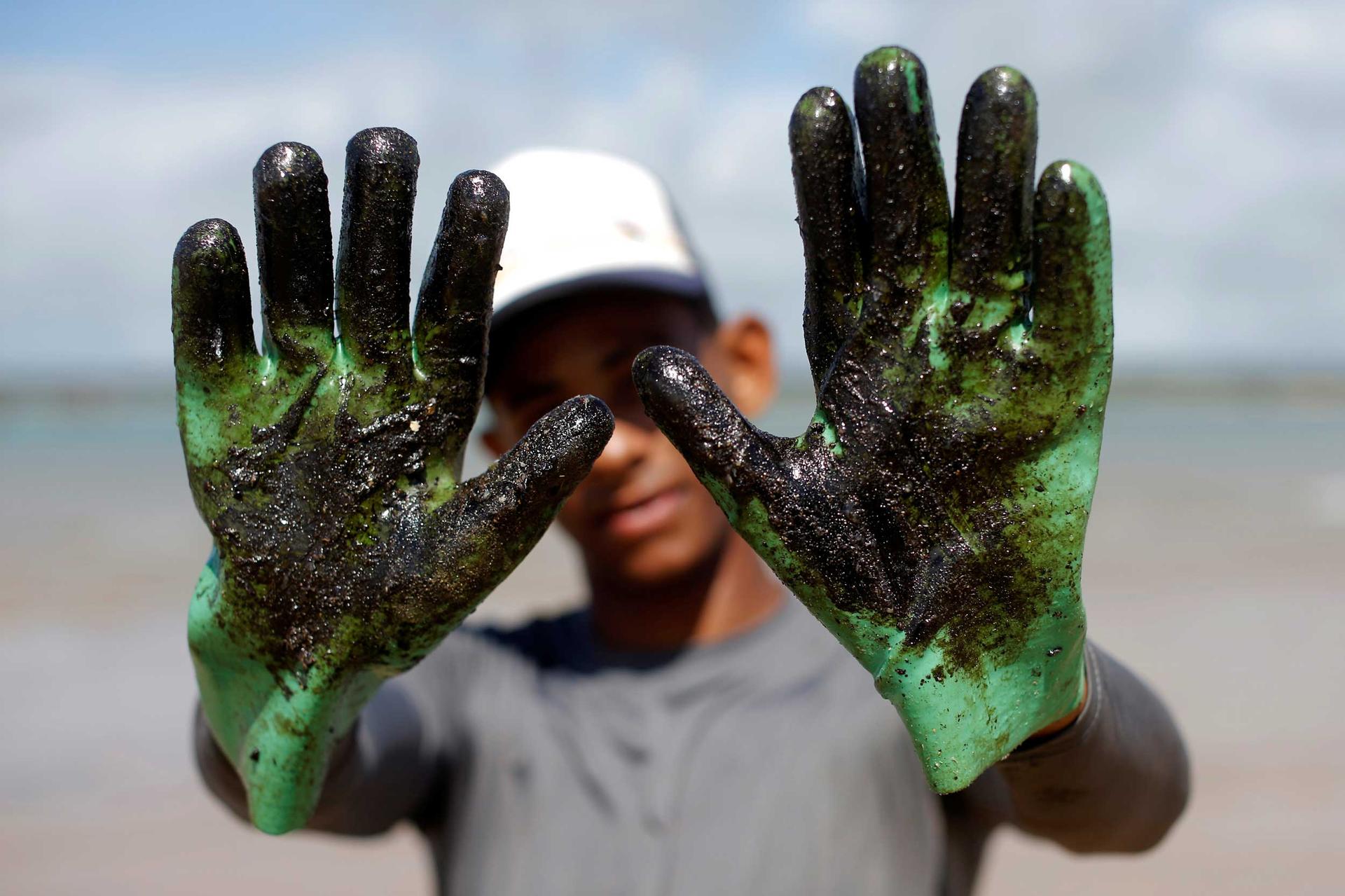 A man holds his hands up to the camera. His green gloves are covered in a sticky, thick, black substance.