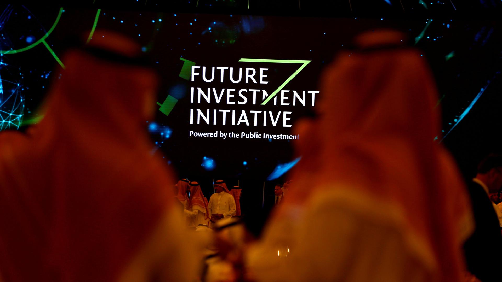 A sign reading "Future Investment Initiative" is visible between the heads of two men