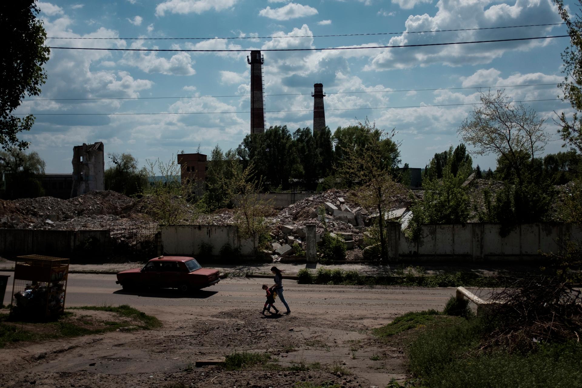 A woman and a child walk amid factory ruins