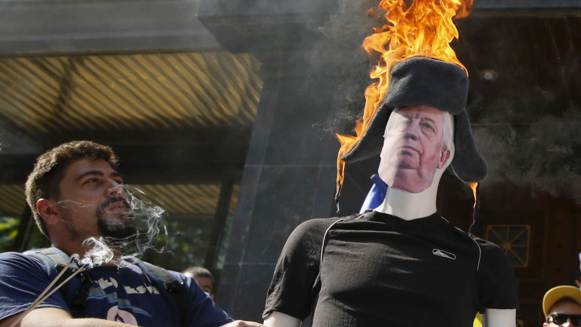 A man stands next to a mannequin with a burning hat. 