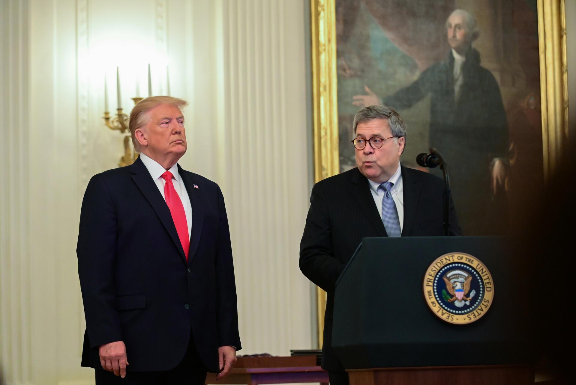 Attorney General William Barr speaks at a lectern while standing beside President Donald Trump.