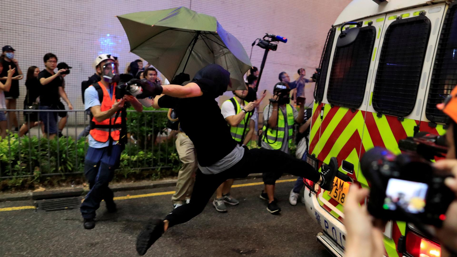 A protester is shown in mid-air kicking a police vehicle with their face fully covered in a mask.