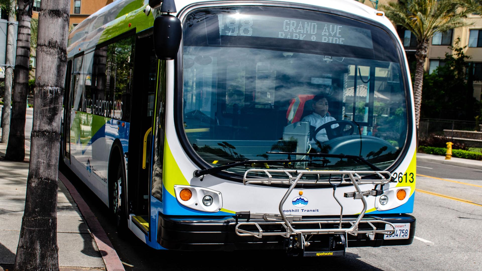 The front of an electric bus is shown with green, blue and white stripes.