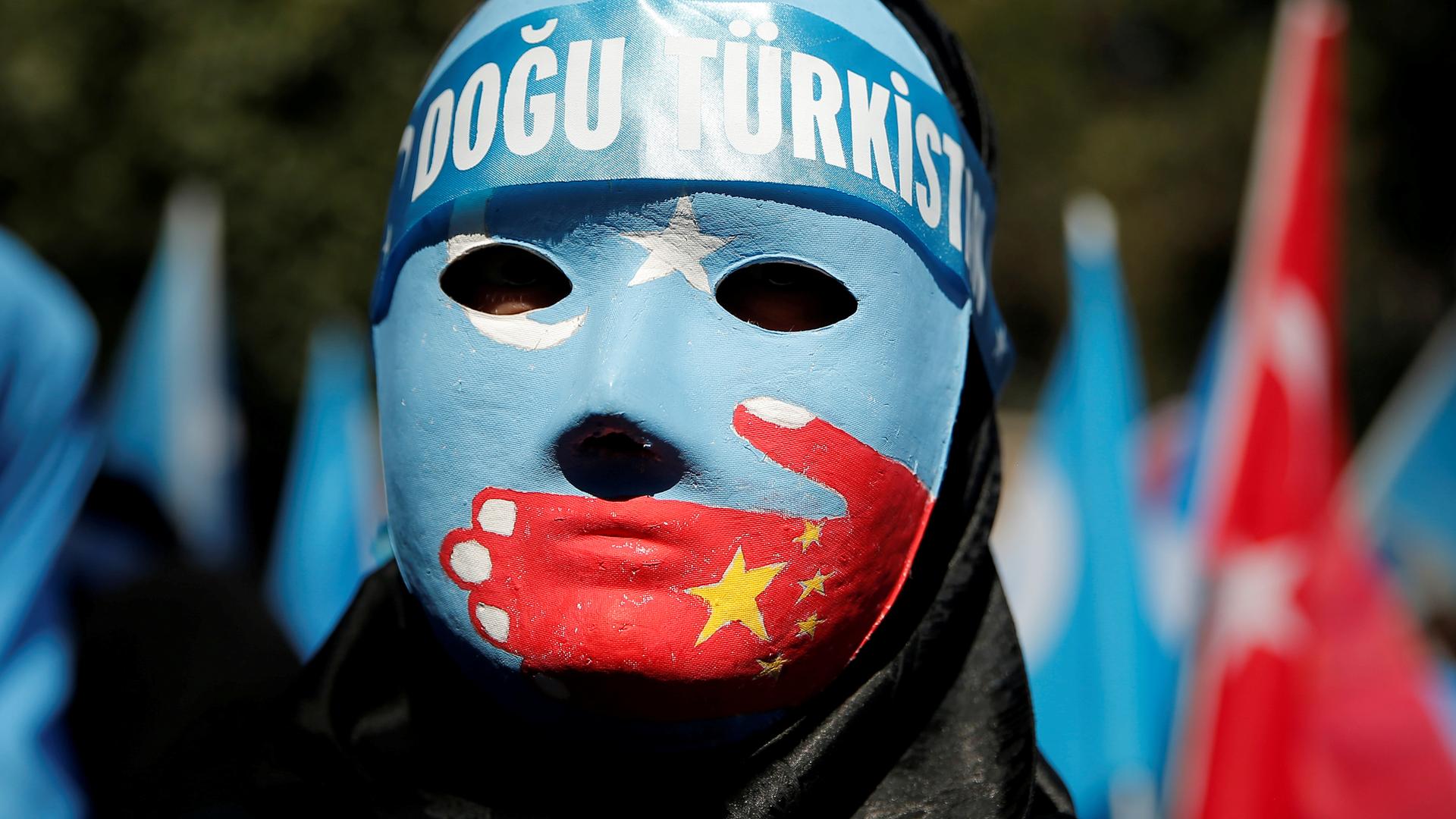 A demonstrator wears a blue mask with a red hand painted across the mouth area. 