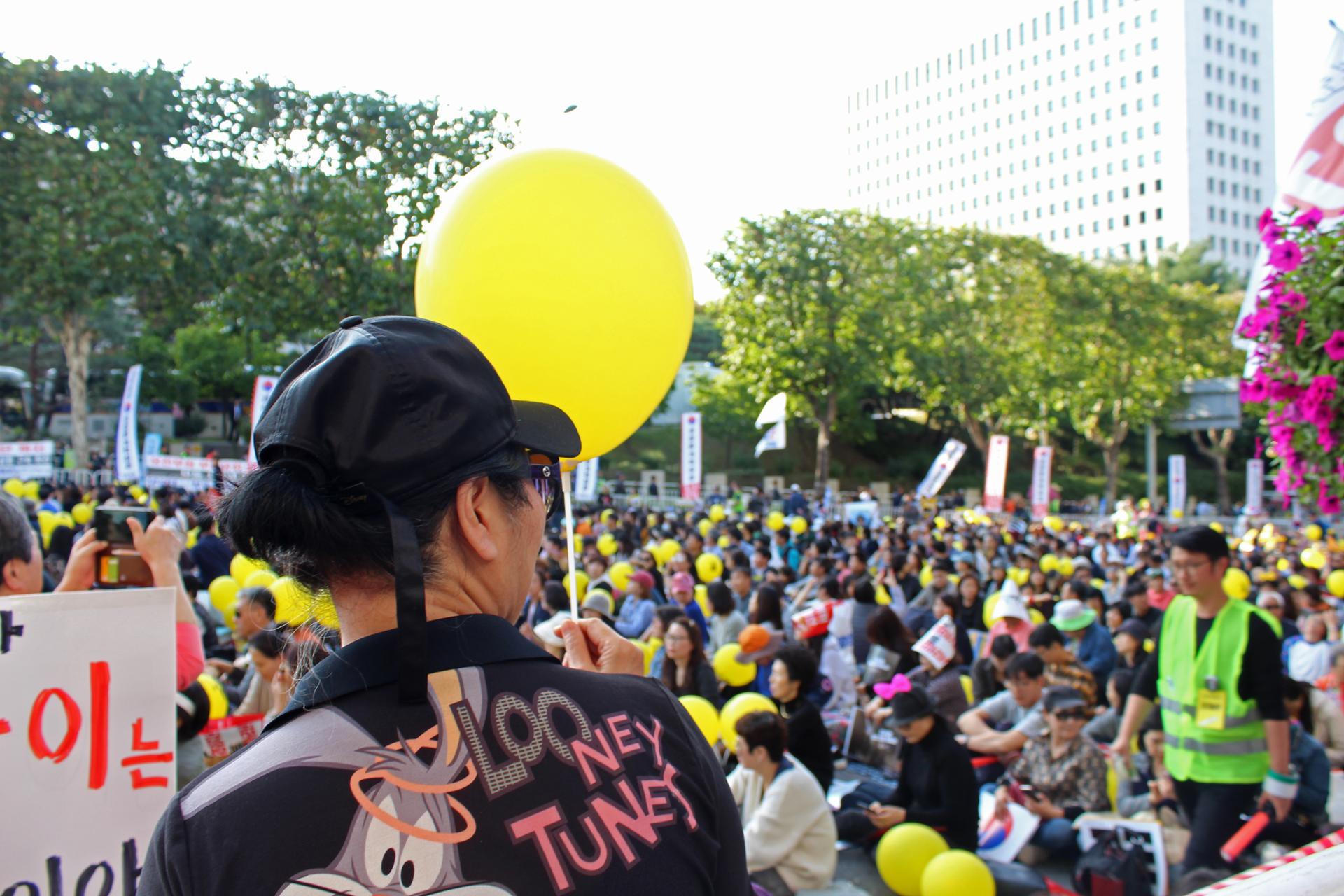Protesters hold up signs in a protest in South Korea holding yellow balloons