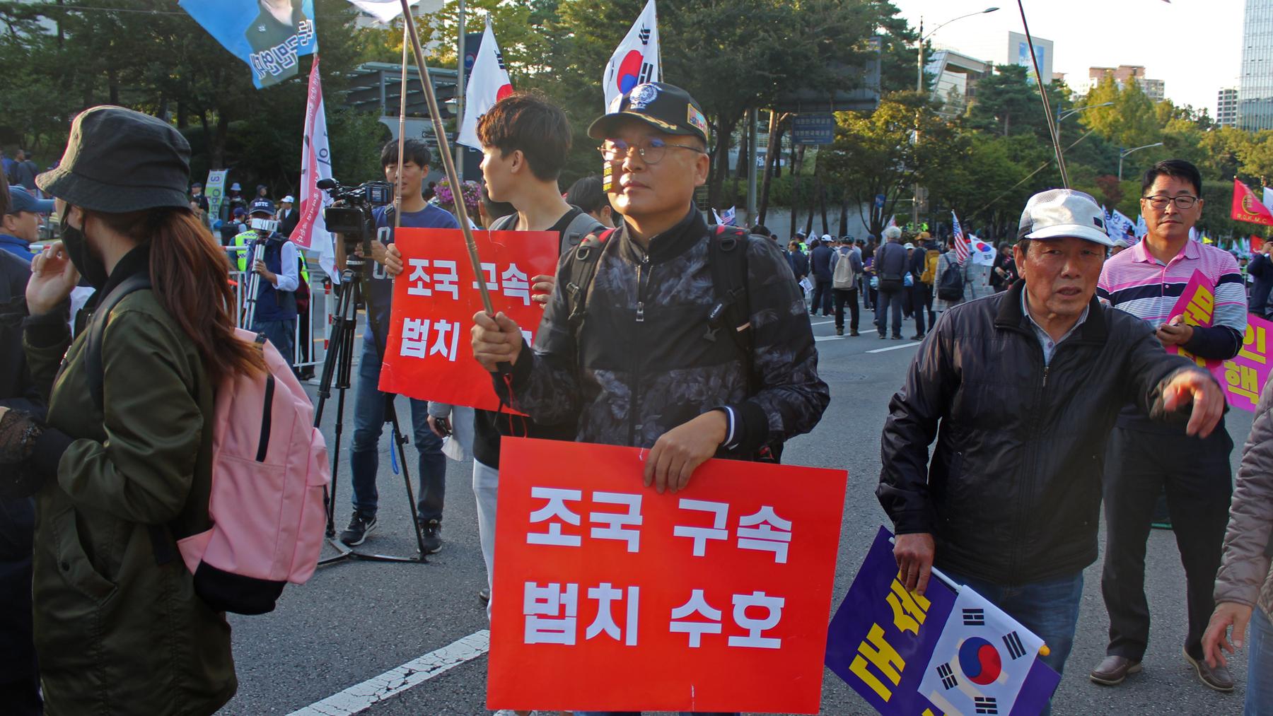 Man stands at protest with red sign and white letters in Korean 
