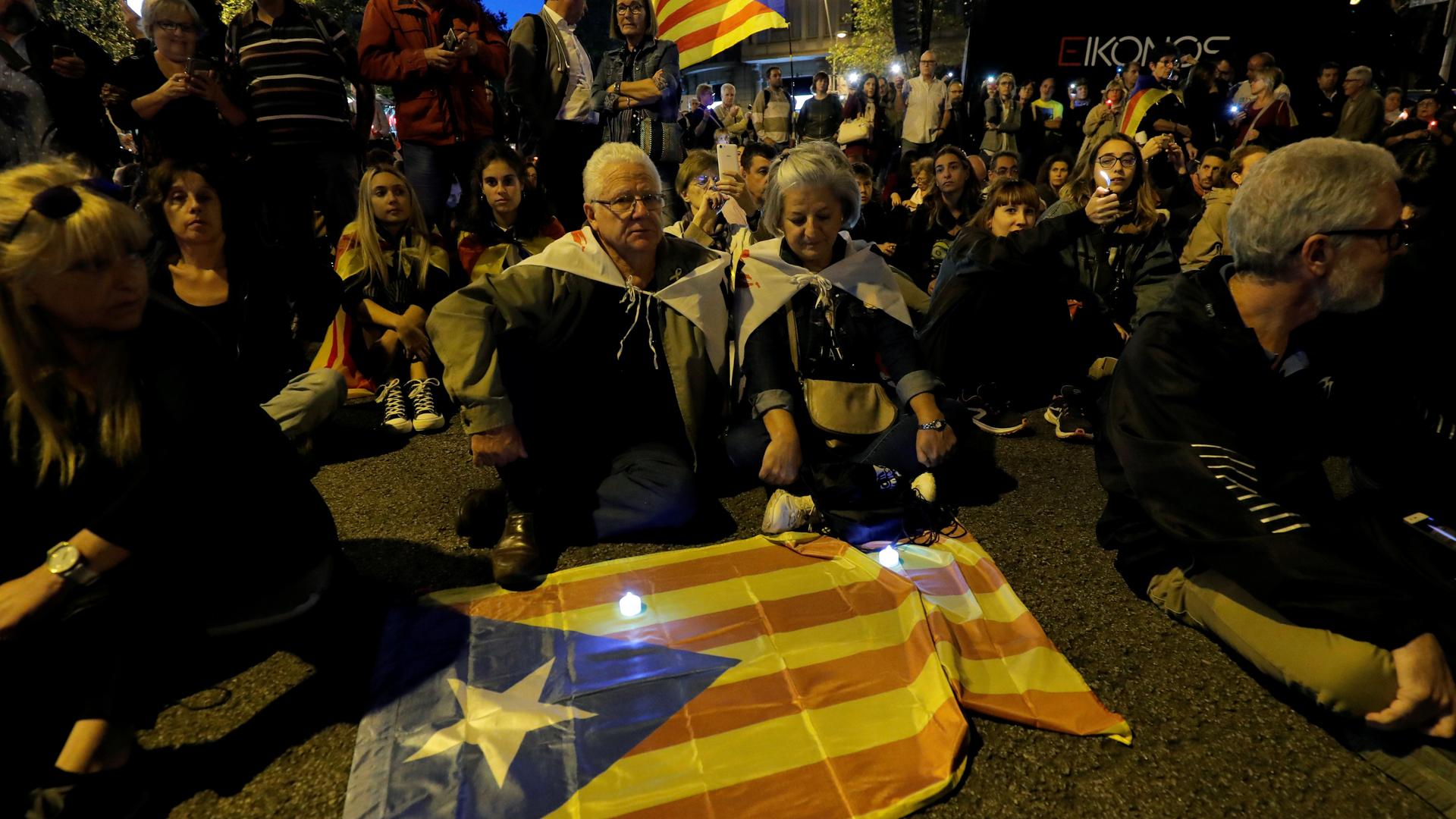 A group of people gather around a flag in a night-time protest with low lights