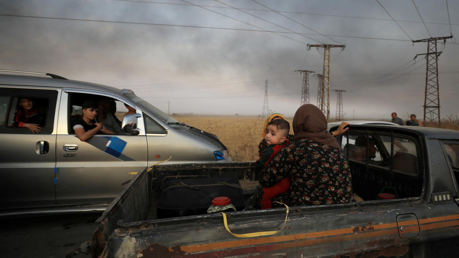 A woman with a baby sits at the back of a truck as they flee Ras al-Ain town, Syria, on Oct. 9, 2019.