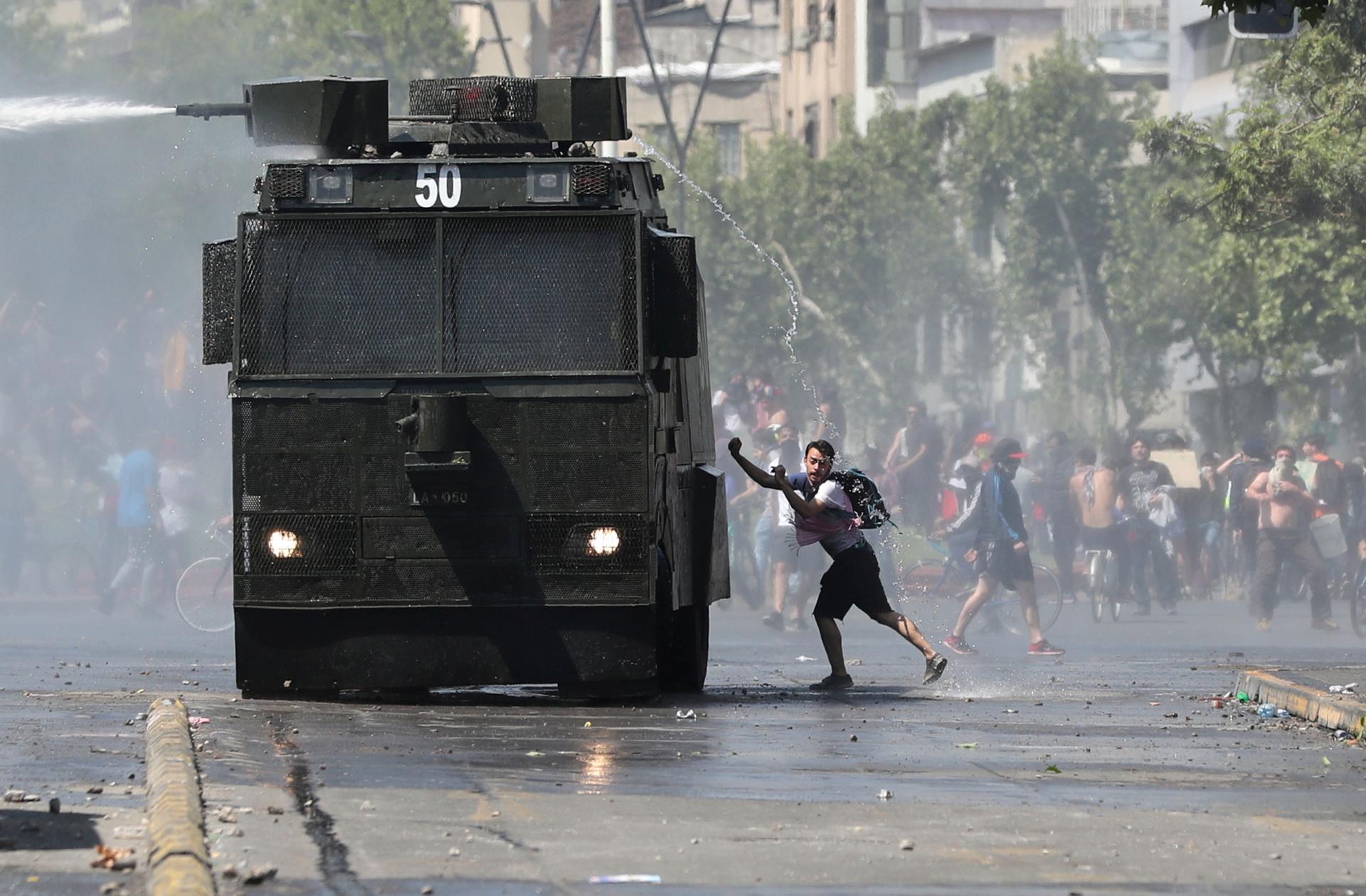 A man is shown wearing shorts and a t-shirt while getting sprayed by a police water cannon from above.
