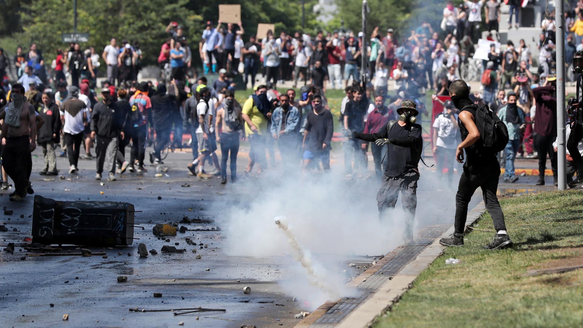 A crowd of demonstrators are shown amassed in the street with a tear gas canister bouncing in the middle of the frame.