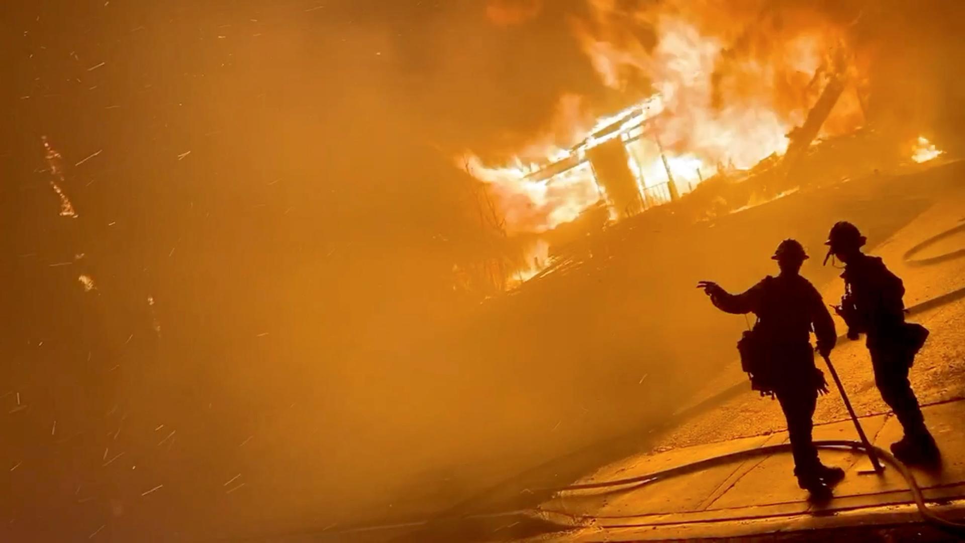 A firefighter gestures to a colleague in front of a house on fire during wildfires in San Bernardino, California, US, on Oct. 31, 2019 in this screen grab obtained from a social media video.