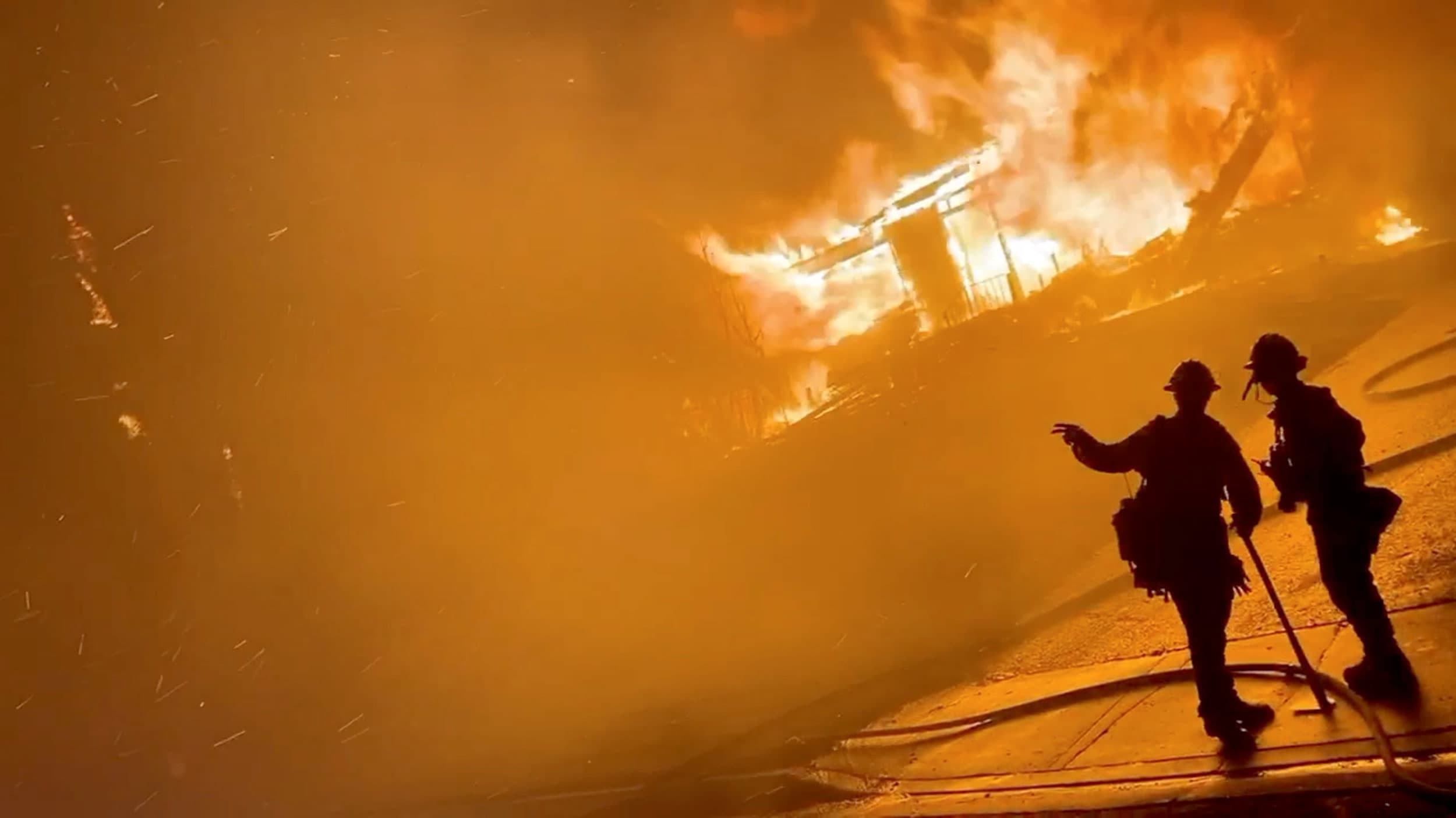 A firefighter gestures to a colleague in front of a house on fire during wildfires in San Bernardino, California, US, on Oct. 31, 2019 in this screen grab obtained from a social media video.