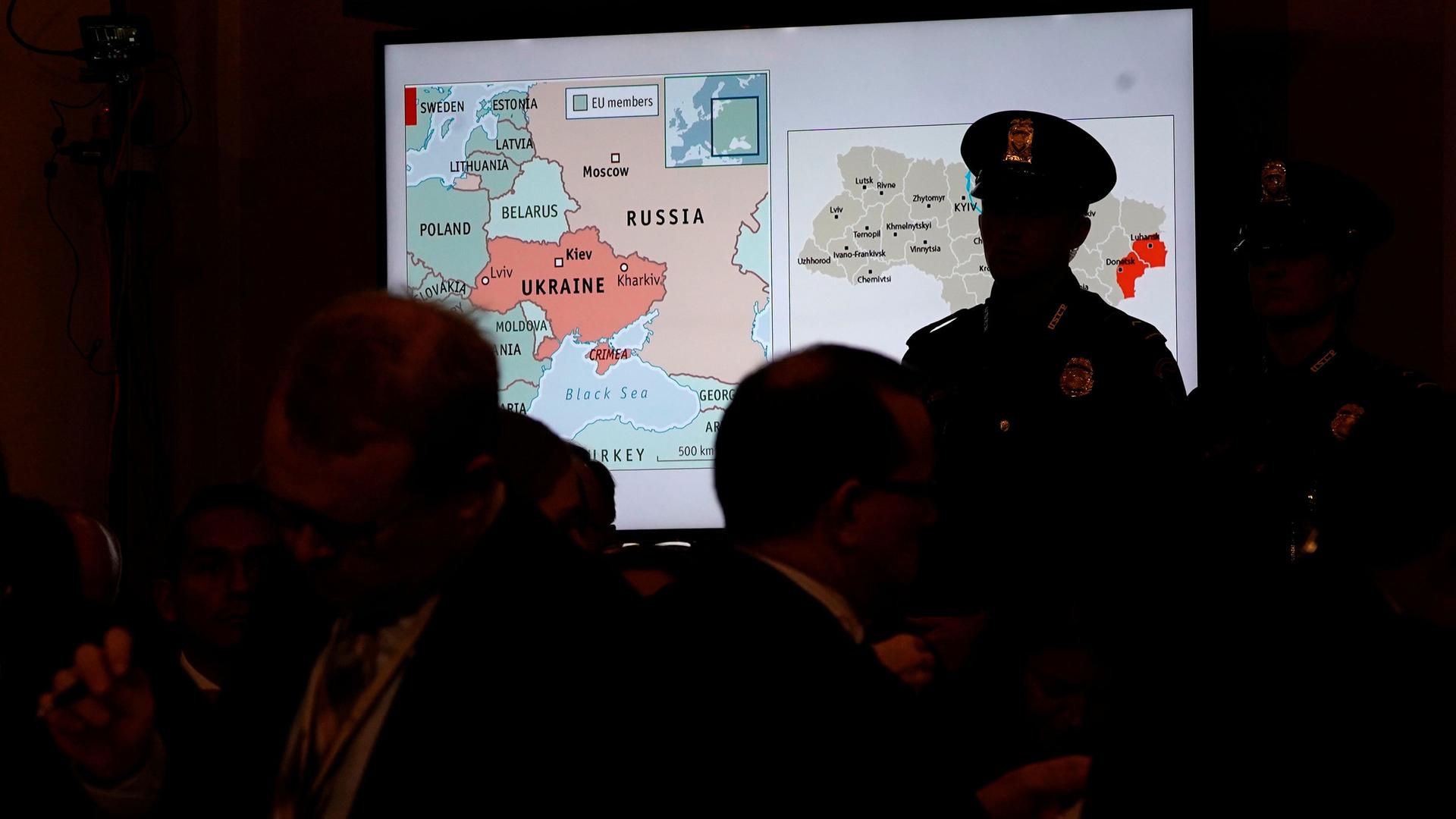 A map of Ukraine is projected onto a screen; a man in a uniform wearing a hat is silhouetted against it.