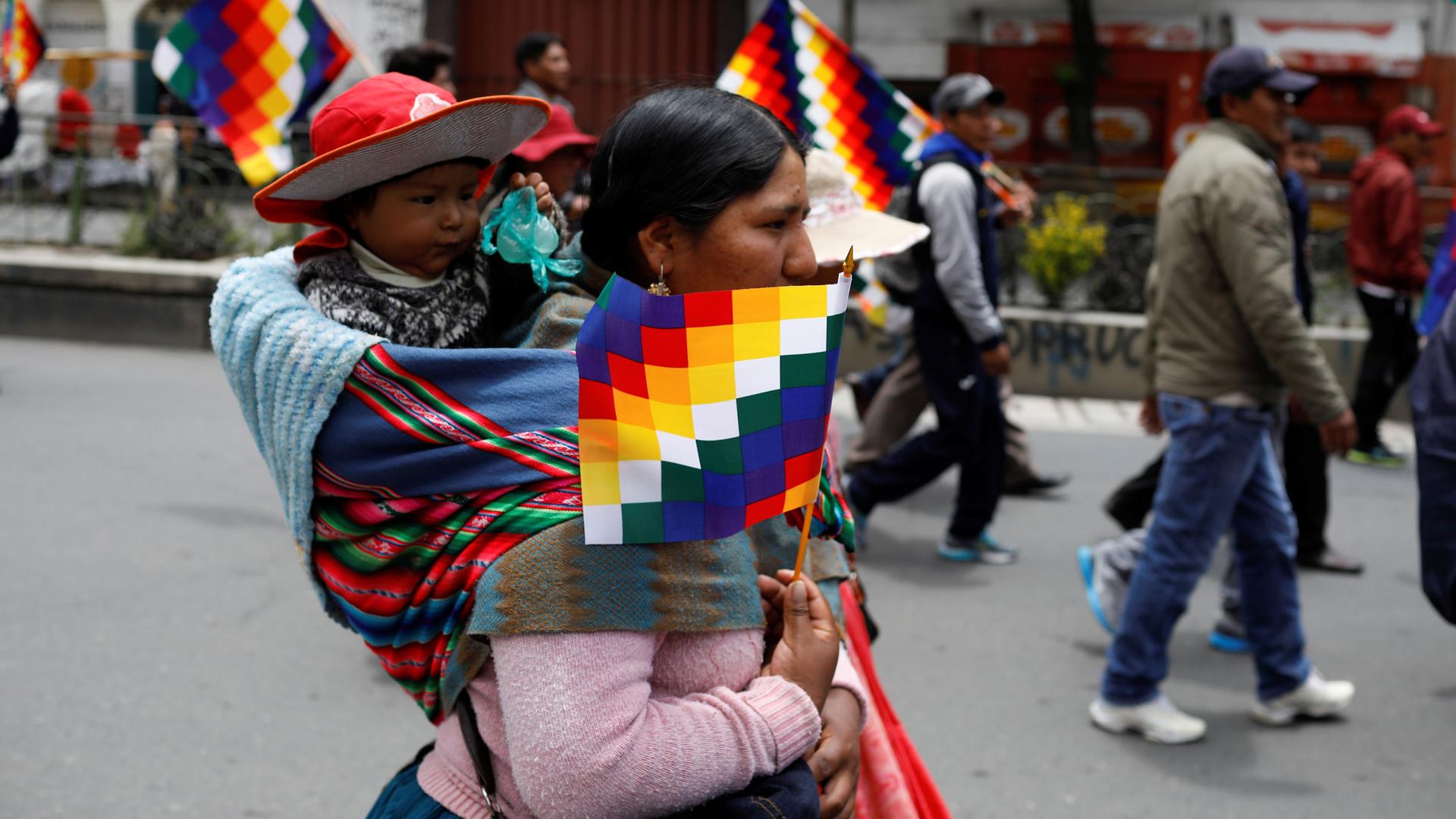An indigenous woman holding a Wiphala flag carries a kid, in La Paz, Bolivia November 13, 2019. 