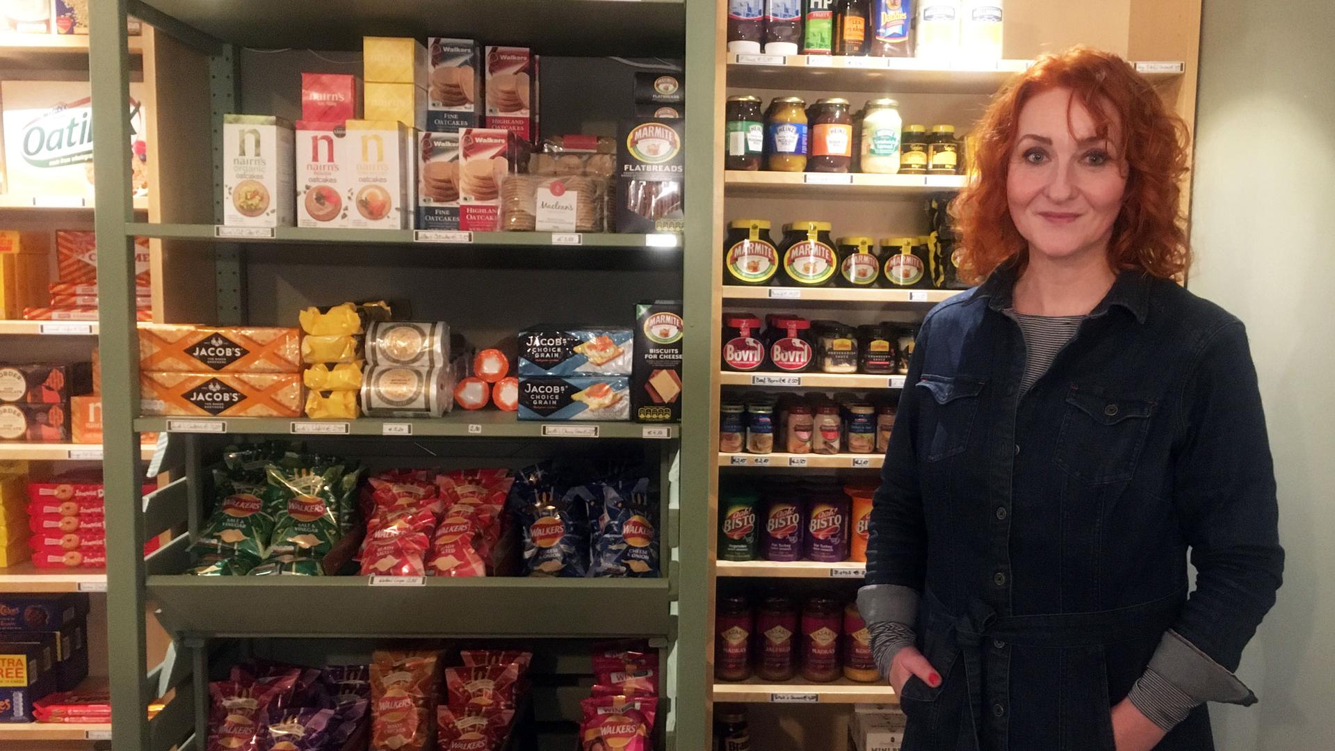 A woman stands by stocked shelfs in a shop