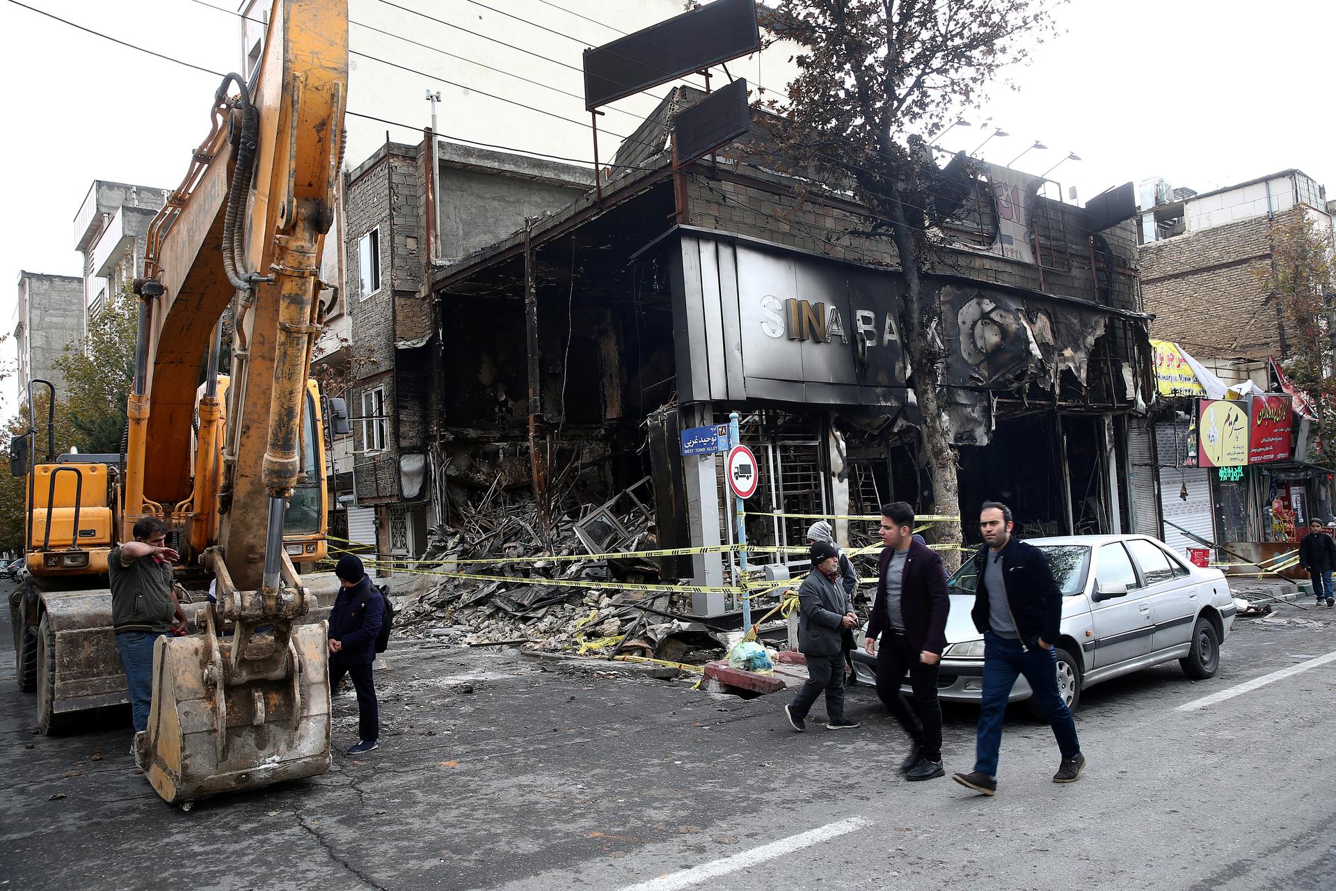 Iranians walk past a burned and destroyed bank.